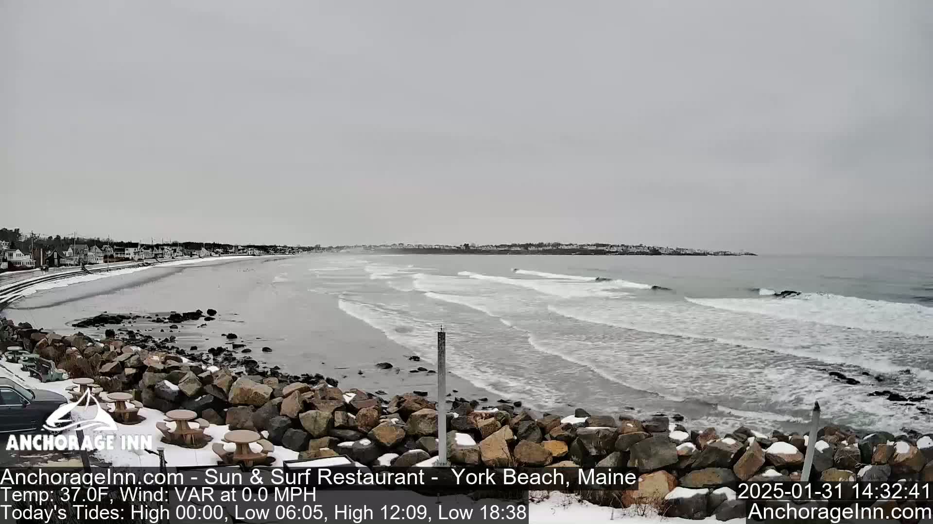 A snowy beach with a rocky shoreline and small waves under an overcast sky.