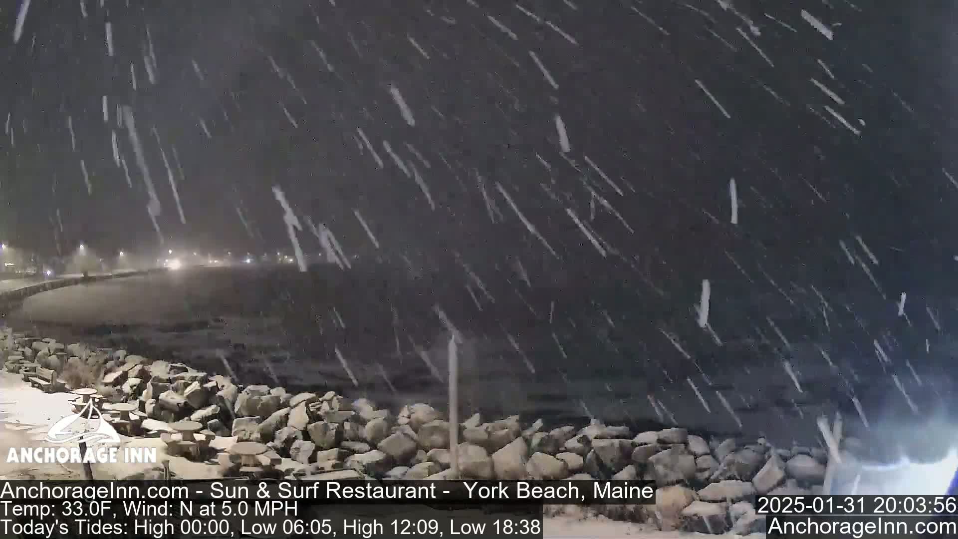 A nighttime scene of heavy snowfall over a rocky shoreline and a dark ocean.
