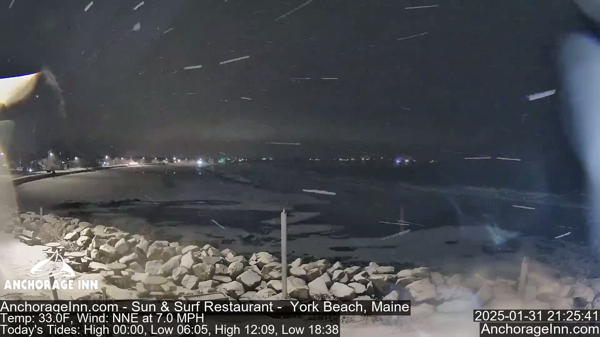 A nighttime scene of a snow-covered shoreline with a body of dark water, under a falling snow.