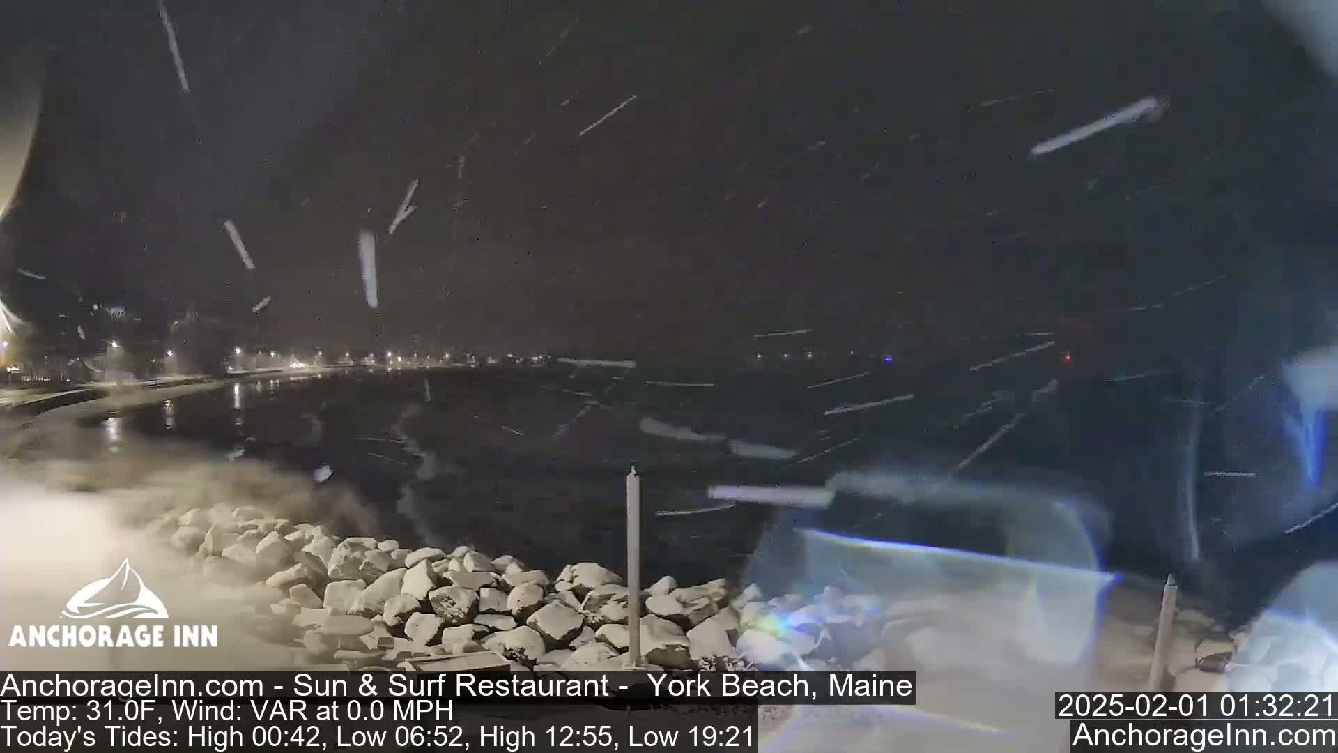 A nighttime scene of a snow-covered rocky shoreline with a dark body of water under heavy snowfall.