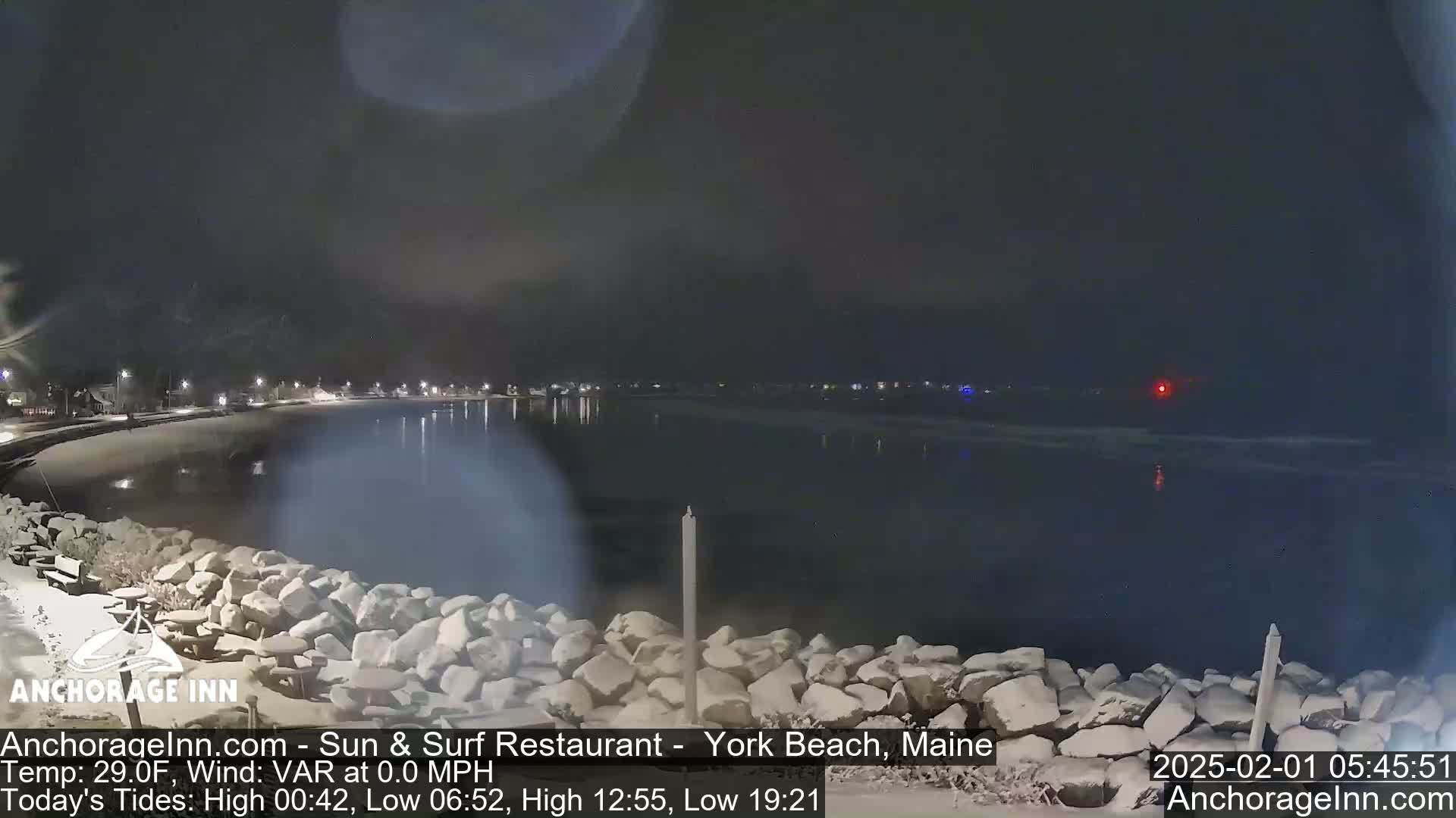 A nighttime view of a snow-covered rocky shoreline and a calm, dark body of water under a cloudy sky.