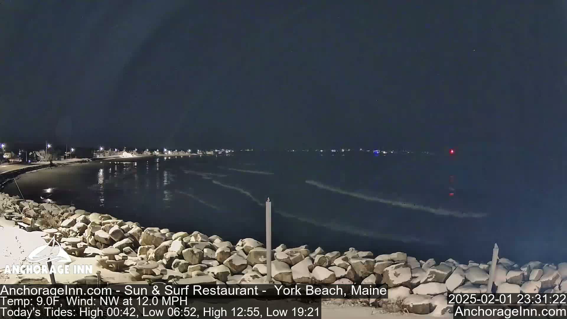 A snow-covered rocky shoreline at night overlooks a dark, wavy ocean under a clear, starlit sky.