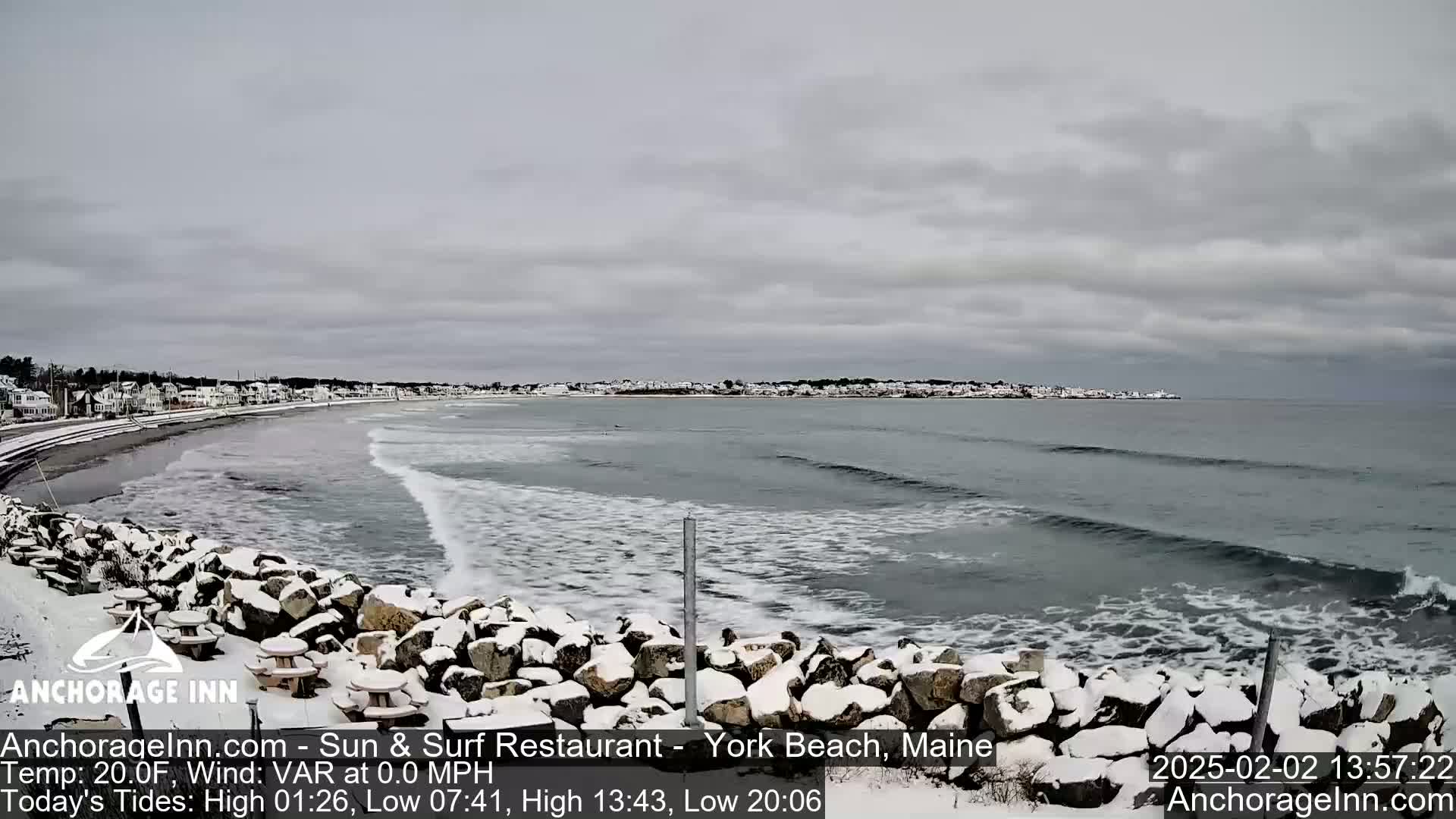 A snow-covered rocky shoreline overlooks a gray, wavy ocean under a cloudy sky.