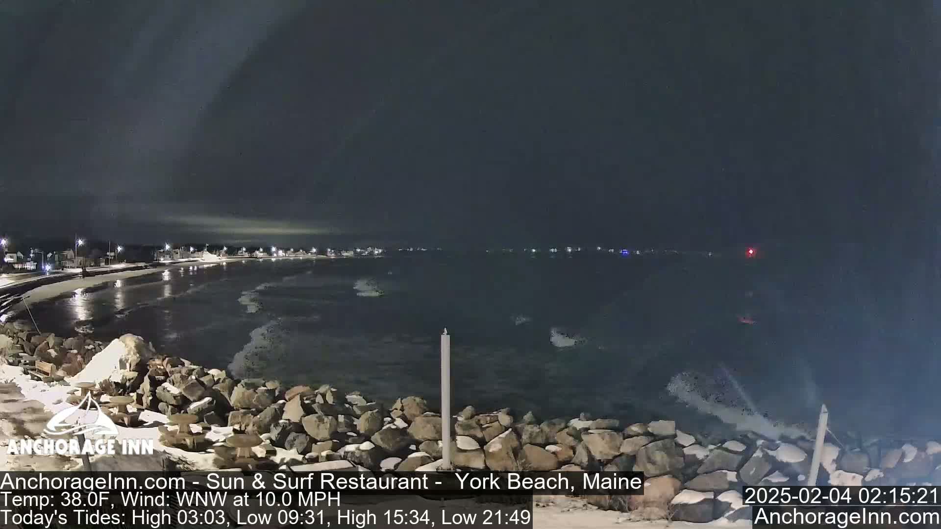 A nighttime view of a rocky shoreline and dark ocean under a cloudy sky.