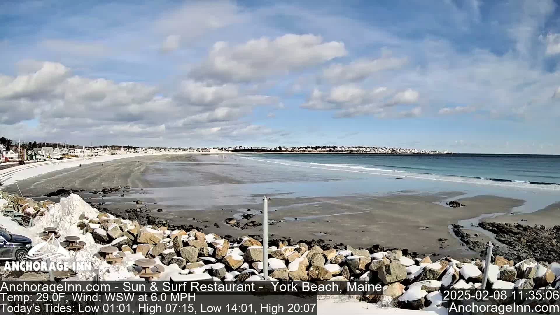A partially snowy beach with a calm ocean under a partly cloudy sky.