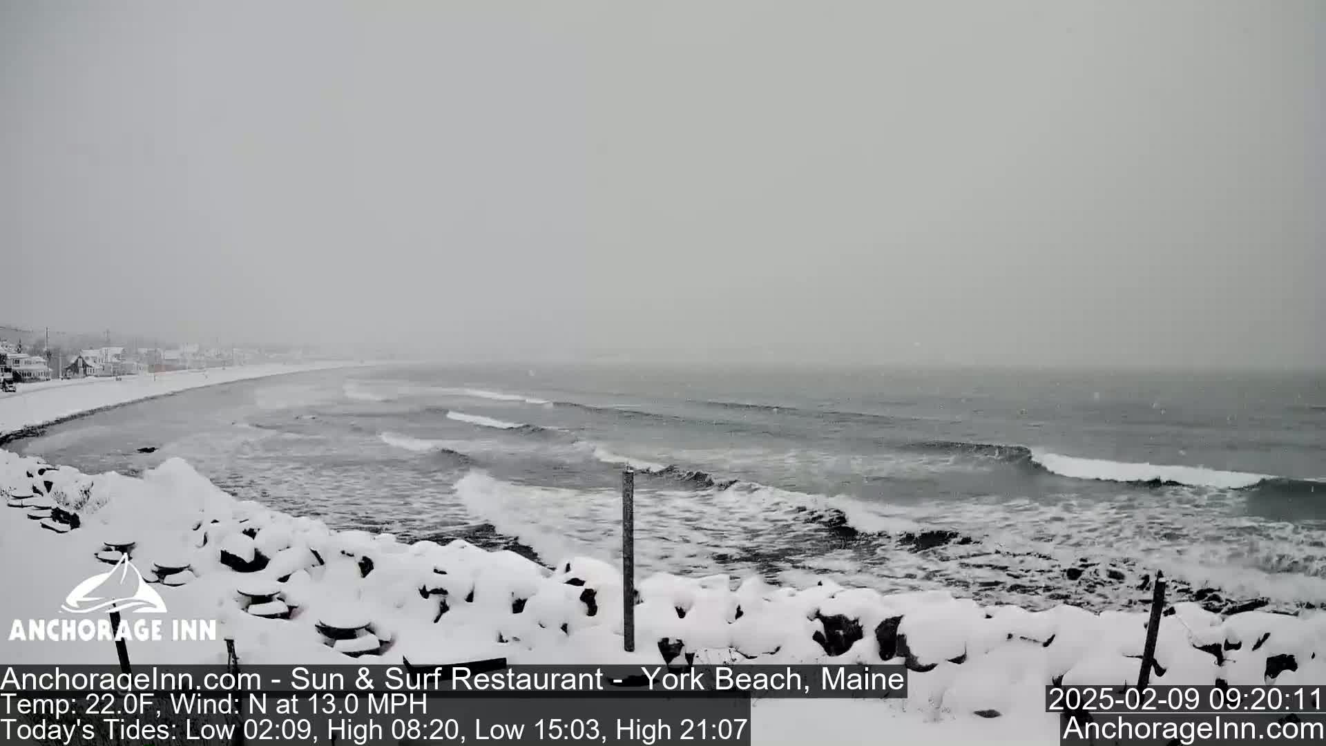 A snow-covered rocky shoreline overlooks a gray, choppy ocean during a snowfall.