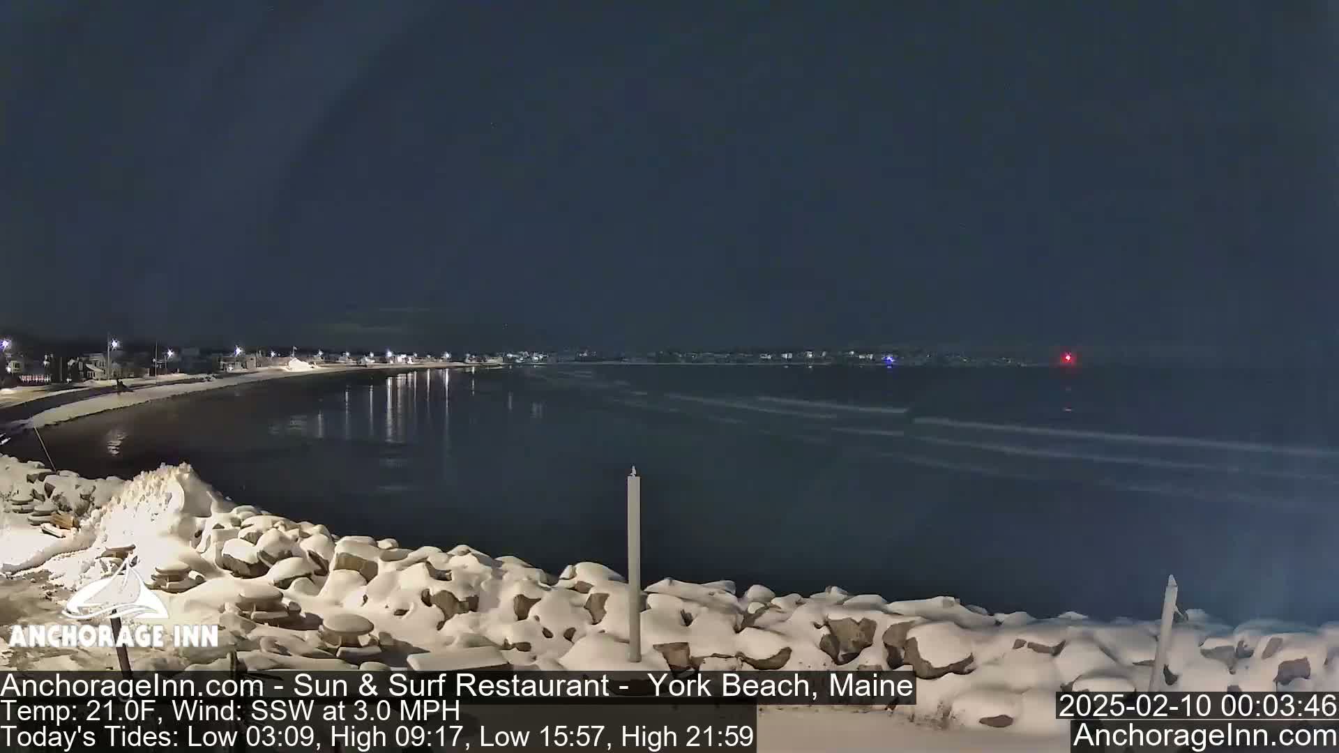 A snow-covered rocky shoreline at night overlooks a dark, calm ocean under a clear sky.