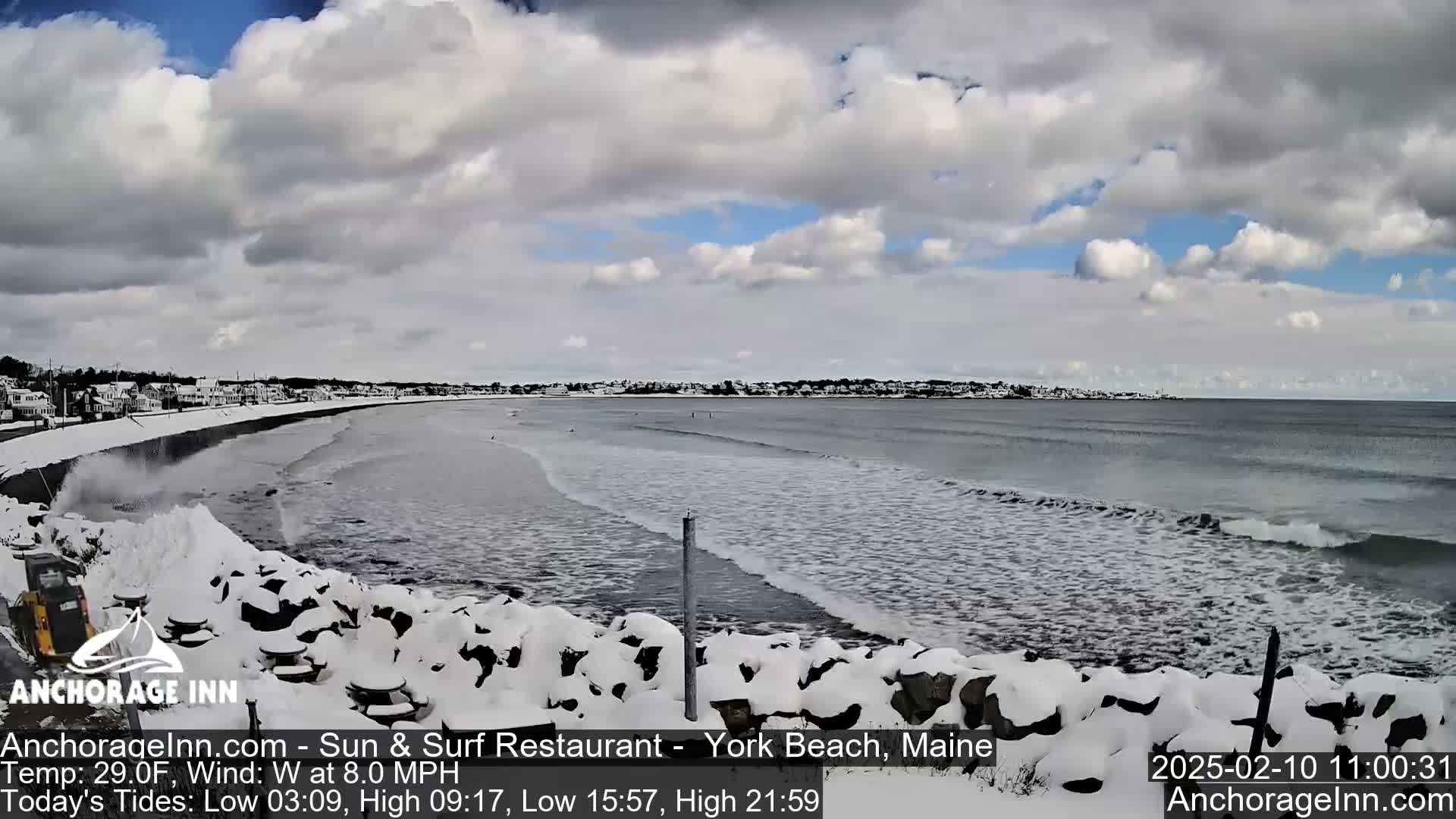 A snow-covered shoreline with a gray, wavy ocean under a cloudy sky.