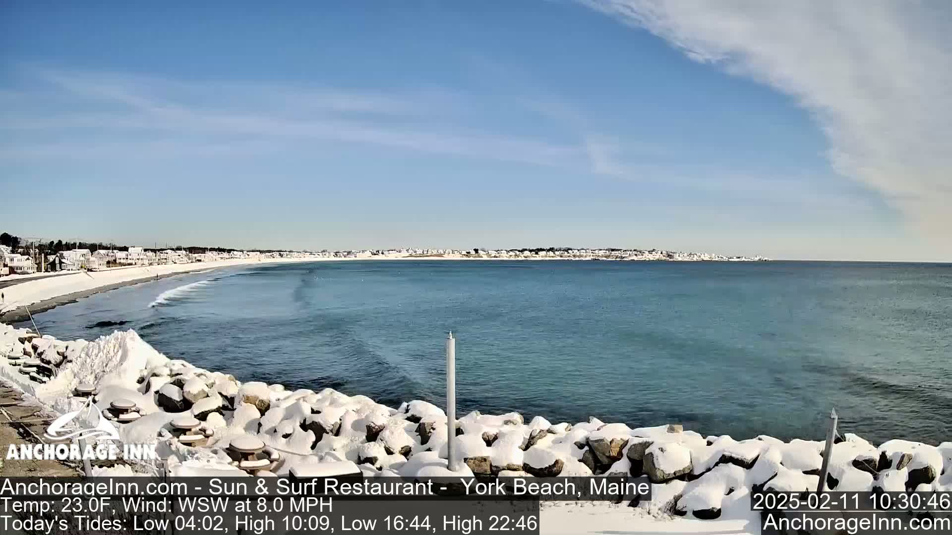 A snow-covered rocky shoreline overlooks a calm ocean with a partly cloudy sky.