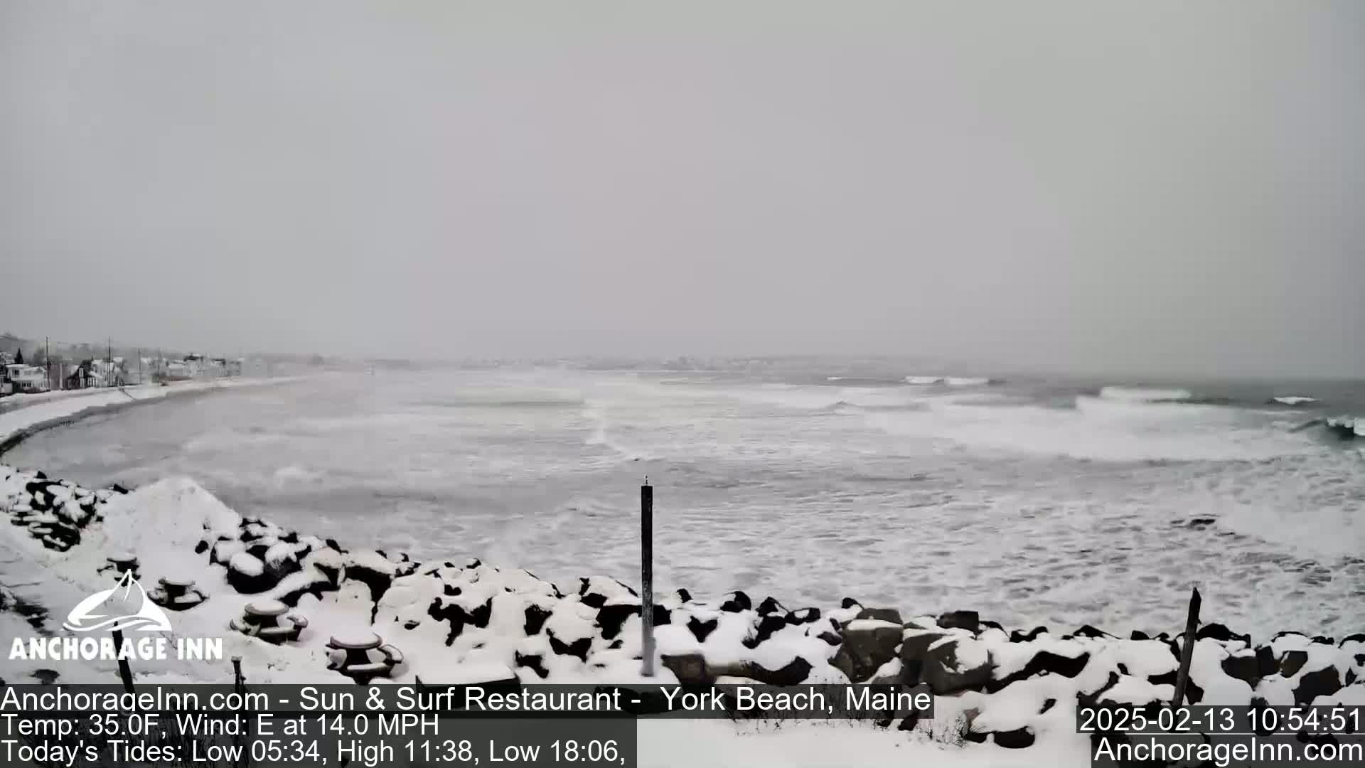 A snow-covered rocky shoreline overlooks a choppy ocean under an overcast sky.