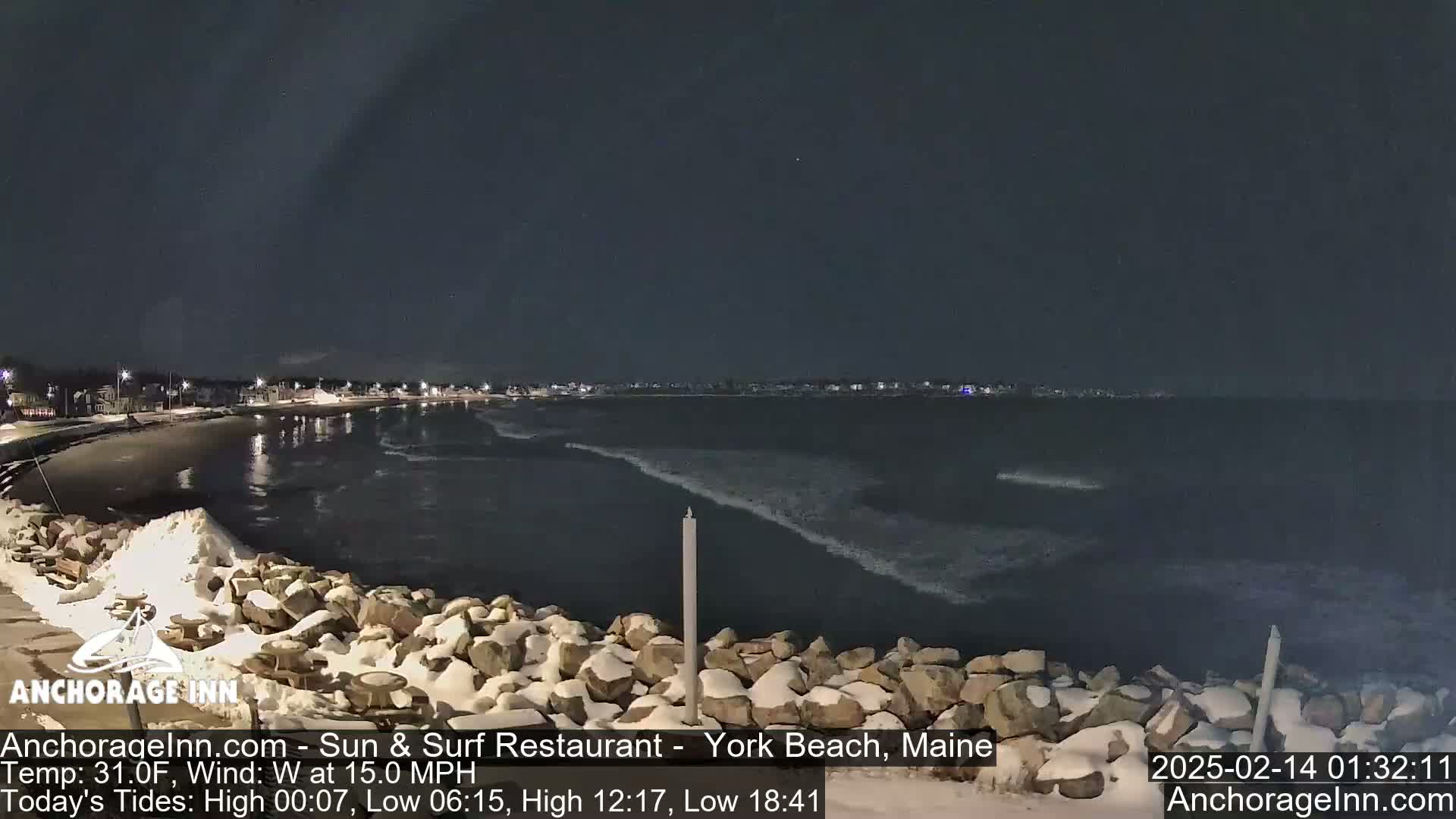 A nighttime view of a snow-dusted rocky shoreline and a dark ocean with small waves under a clear, dark sky.