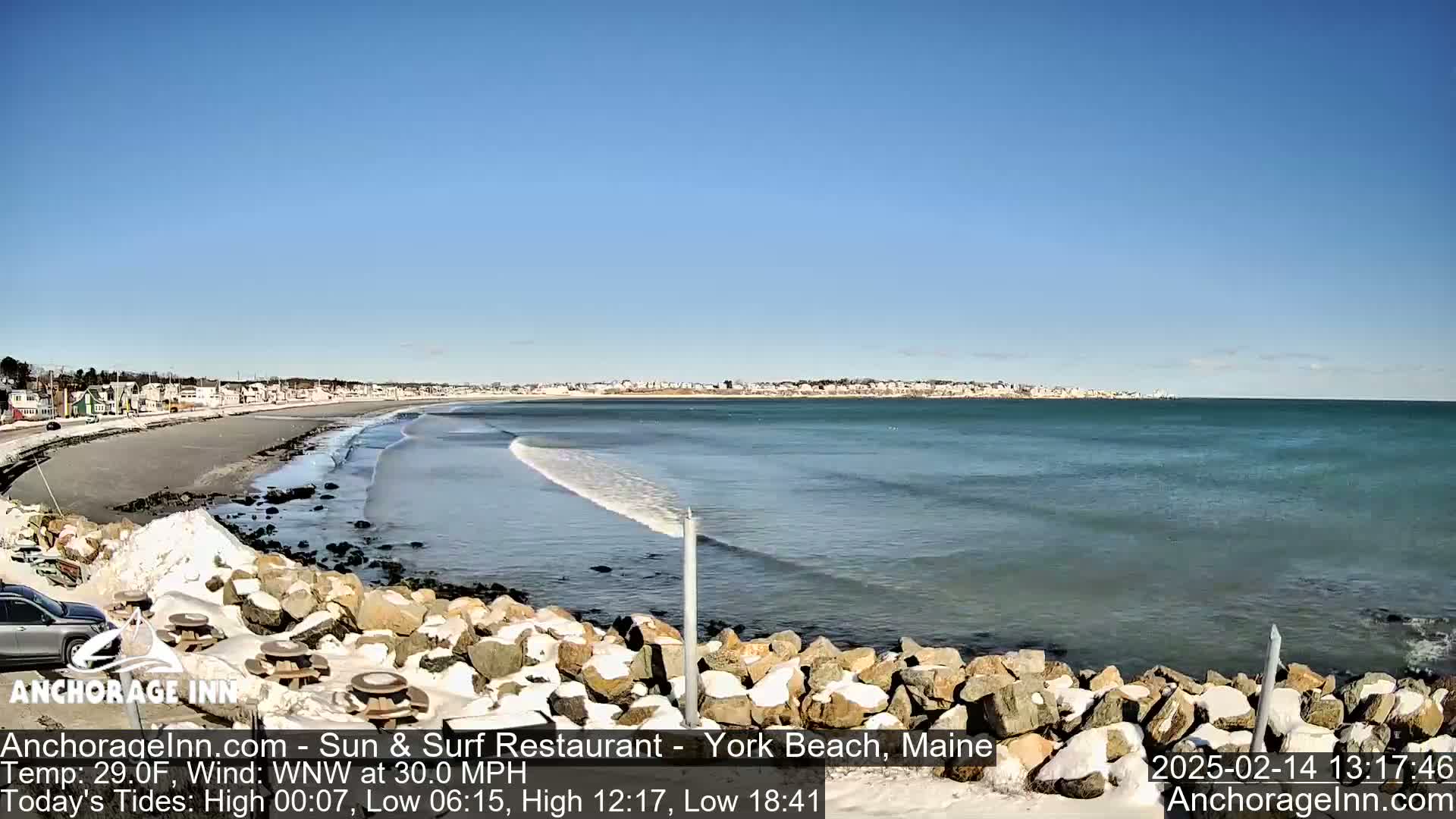 A partly sunny day at a rocky beach with light snow on the ground and small waves in the ocean.