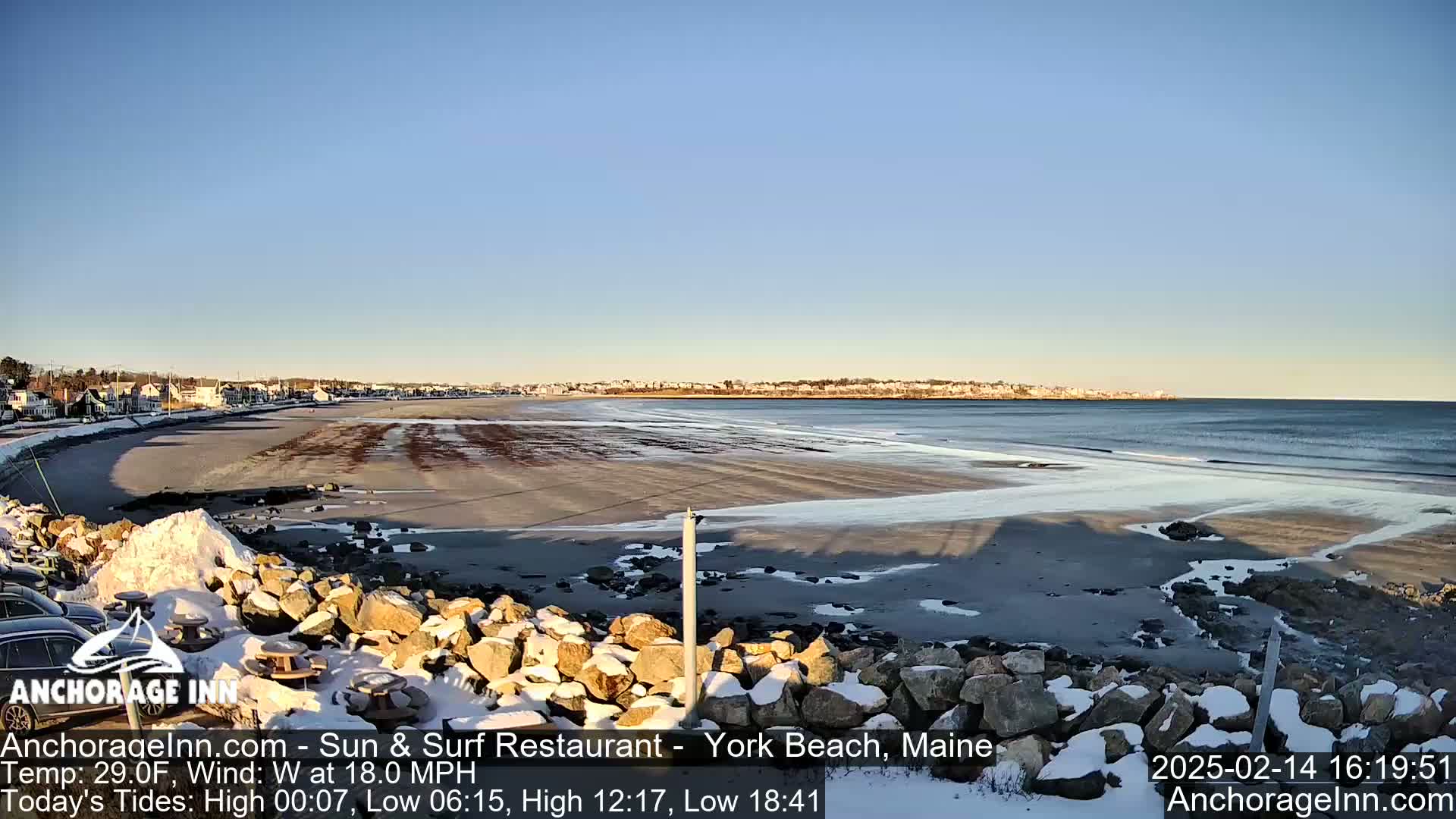 A partly-snowy beach with a calm ocean under a clear blue sky.