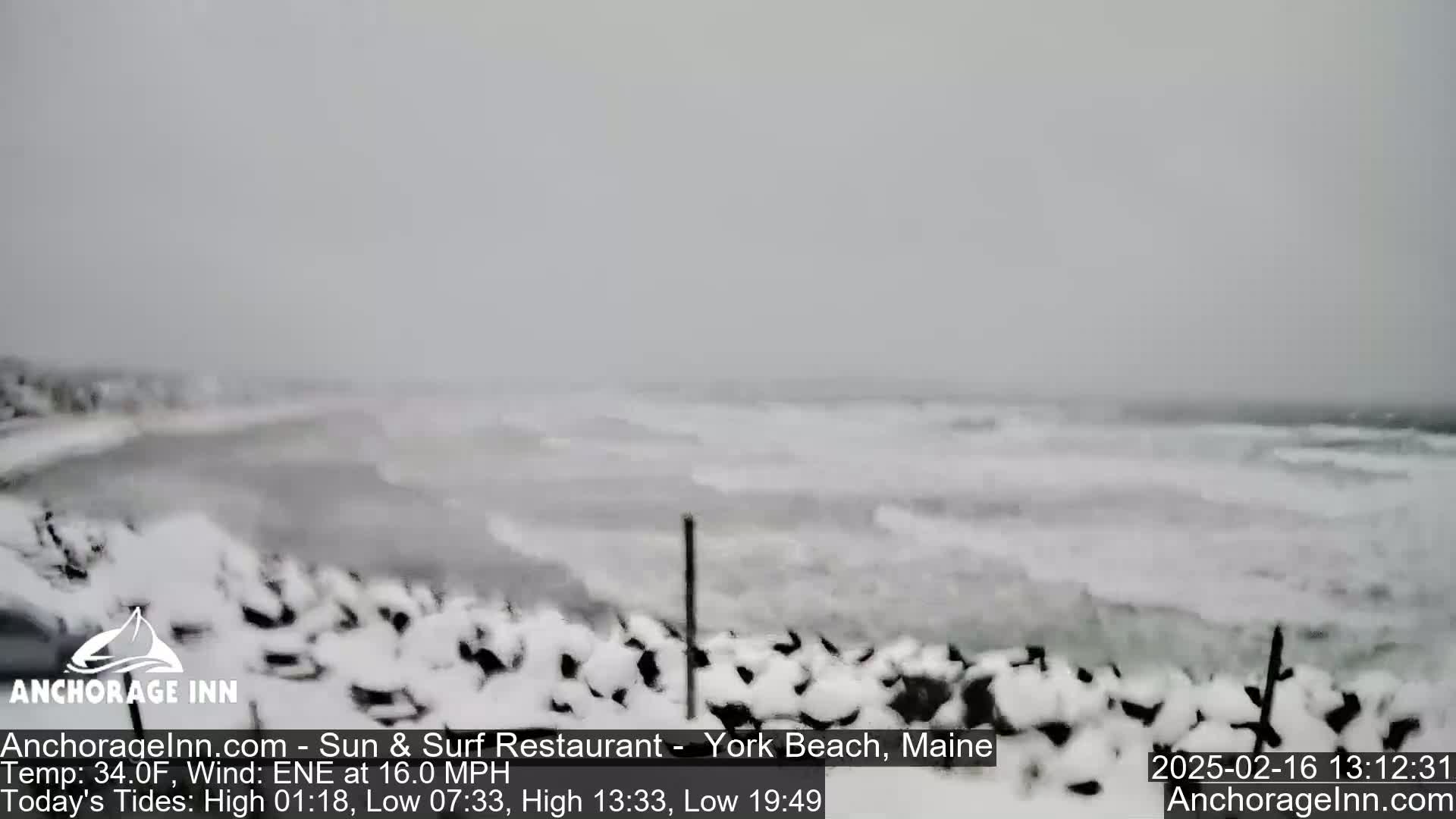 A snow-covered rocky shoreline is battered by choppy waves during a snowstorm.