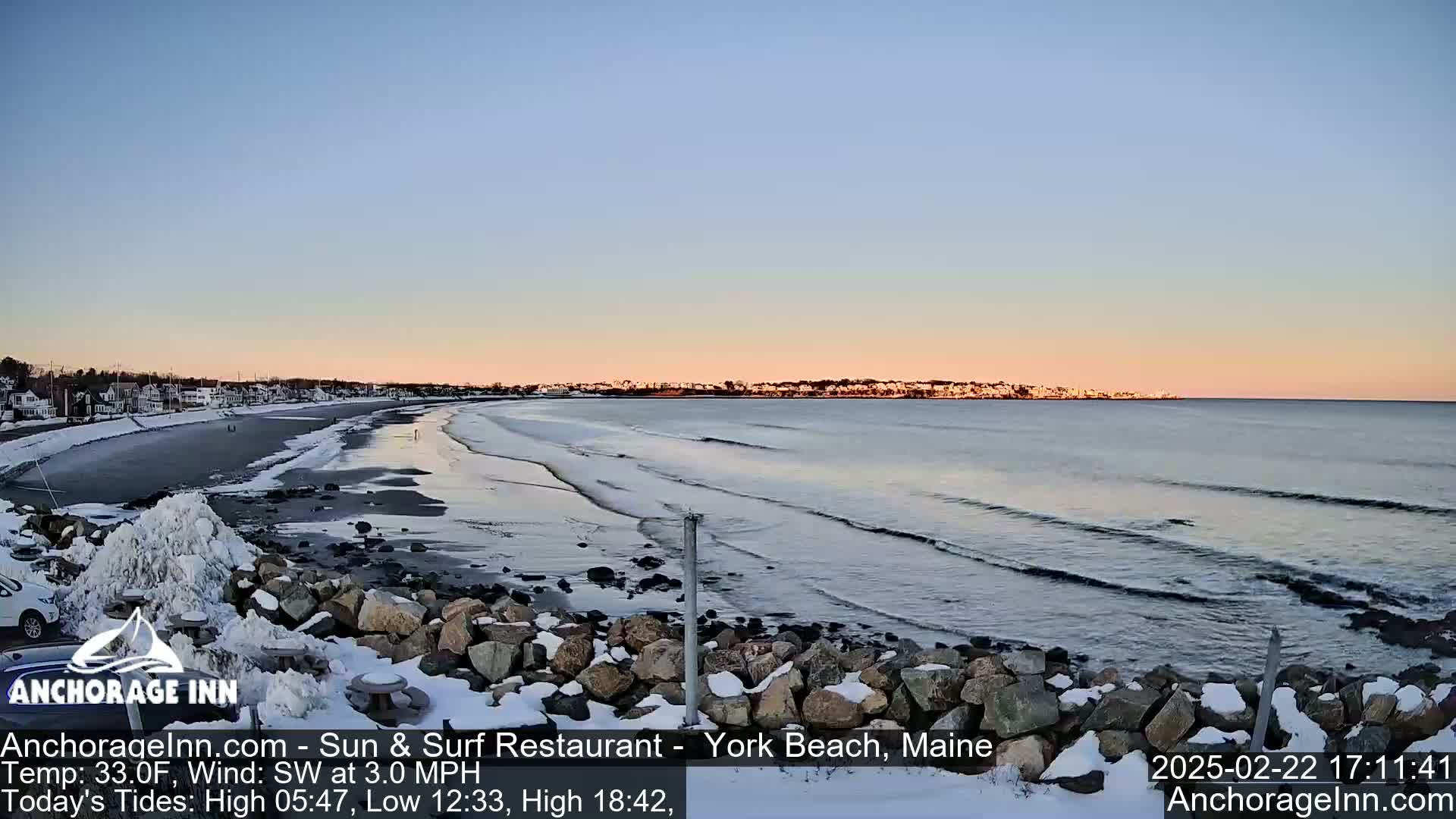 A snow-dusted rocky shoreline meets a calm ocean with gentle waves under a twilight sky.