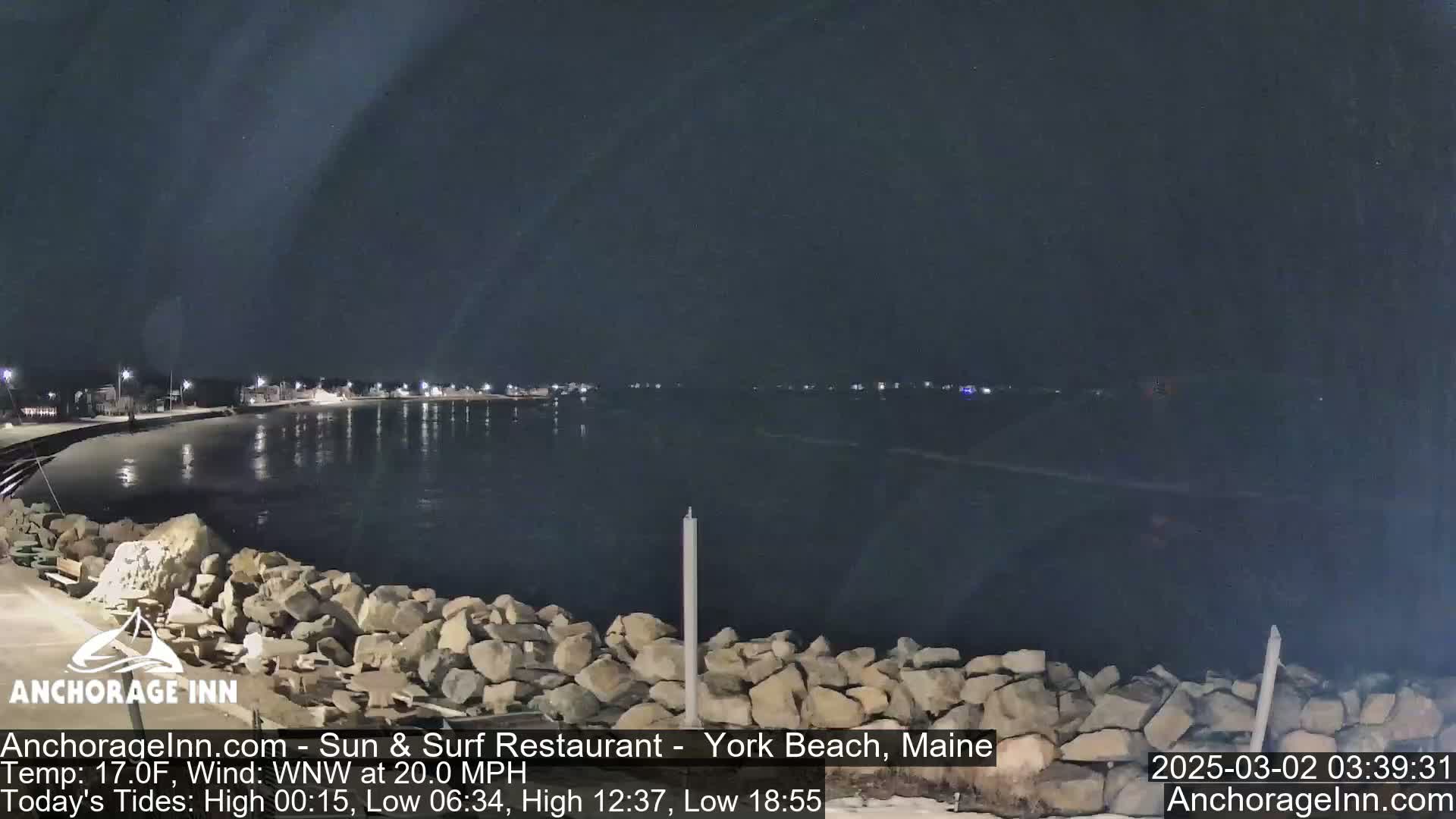 A nighttime view of a calm, dark body of water next to a rocky shoreline under a clear, dark sky.