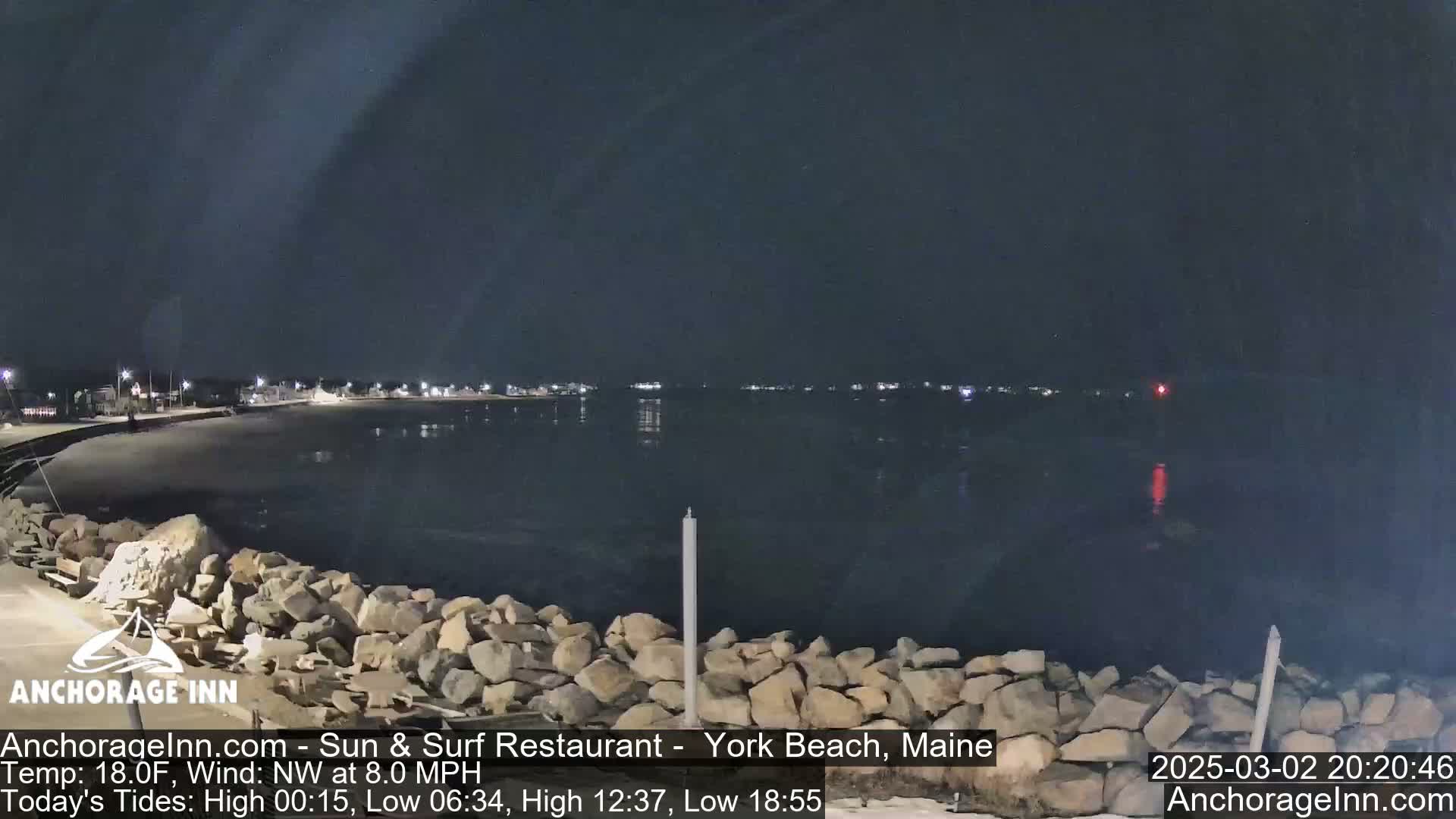 A nighttime view of a rocky shoreline and calm ocean, under a dark sky.