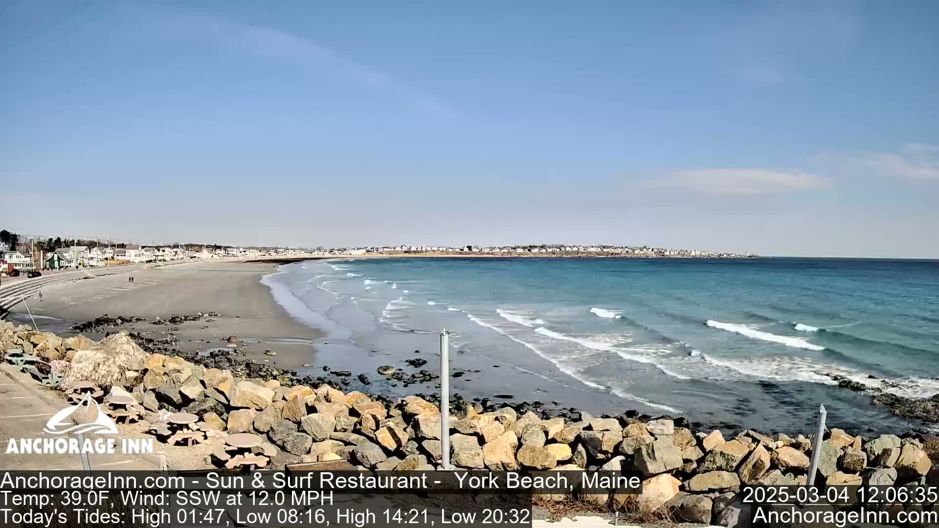 A sandy beach with small waves laps a rocky shore under a clear blue sky.