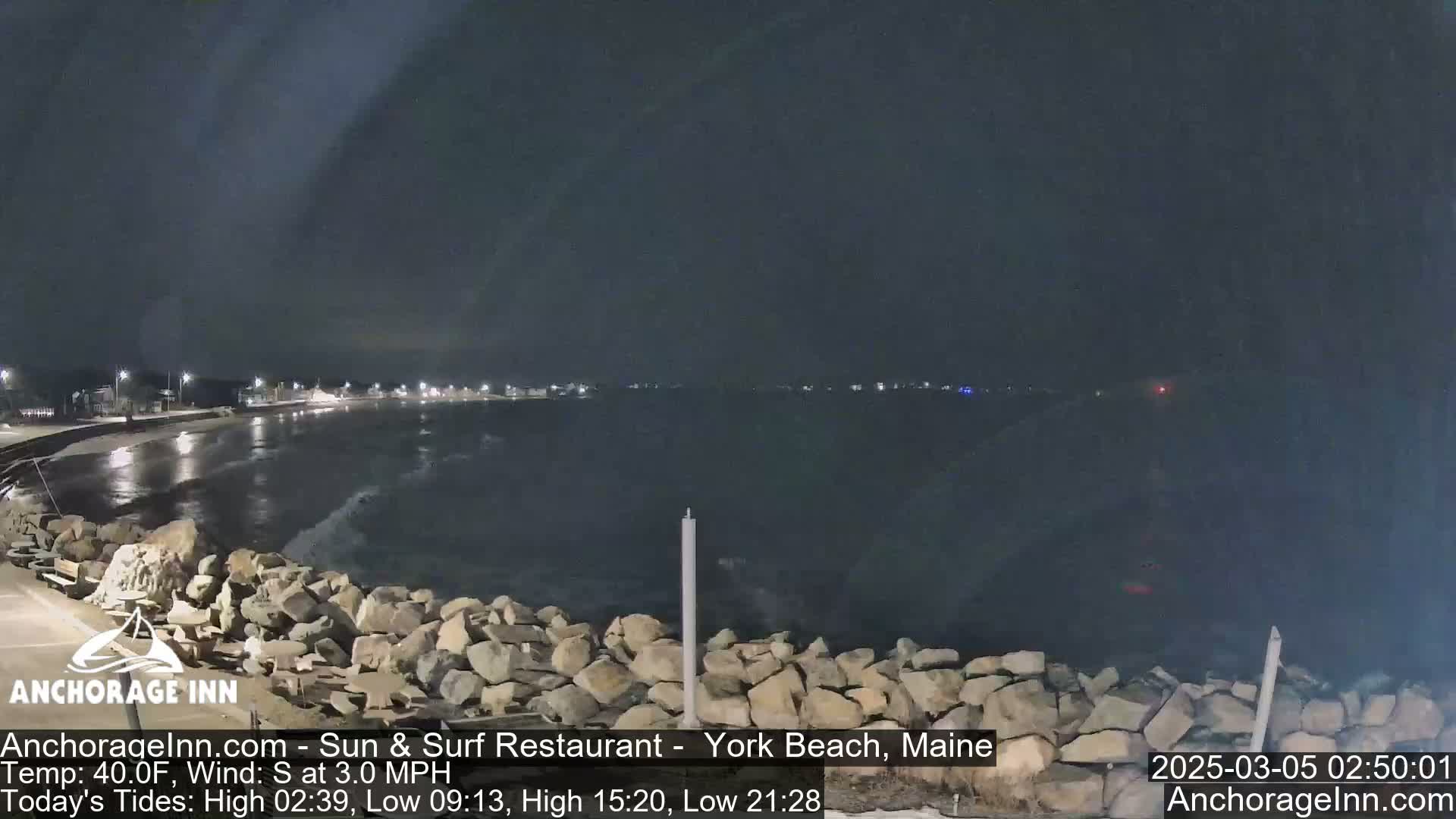 A nighttime view of a rocky shoreline and calm ocean under a dark sky.