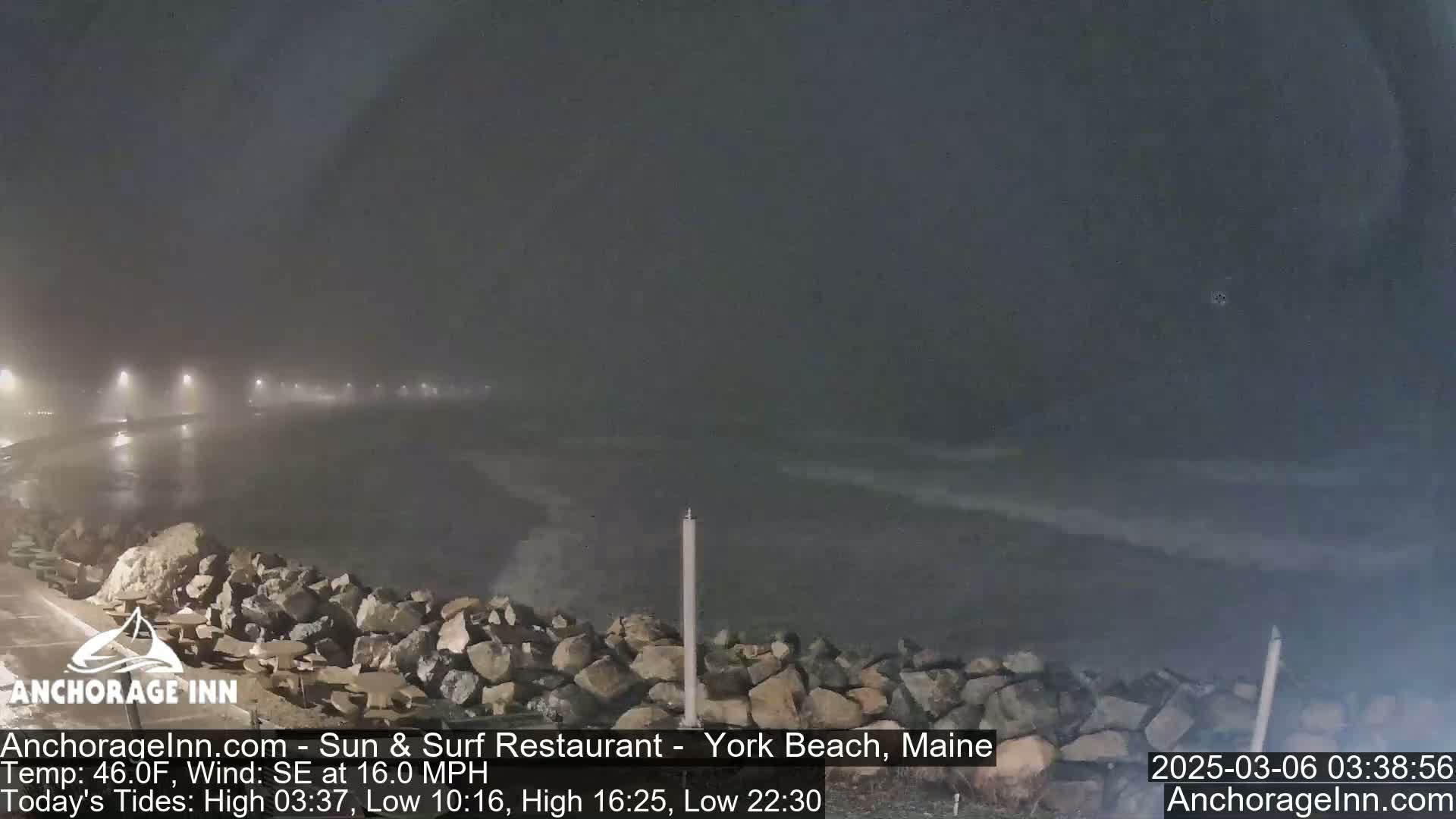A nighttime view of a rocky shoreline and choppy ocean water under foggy conditions.