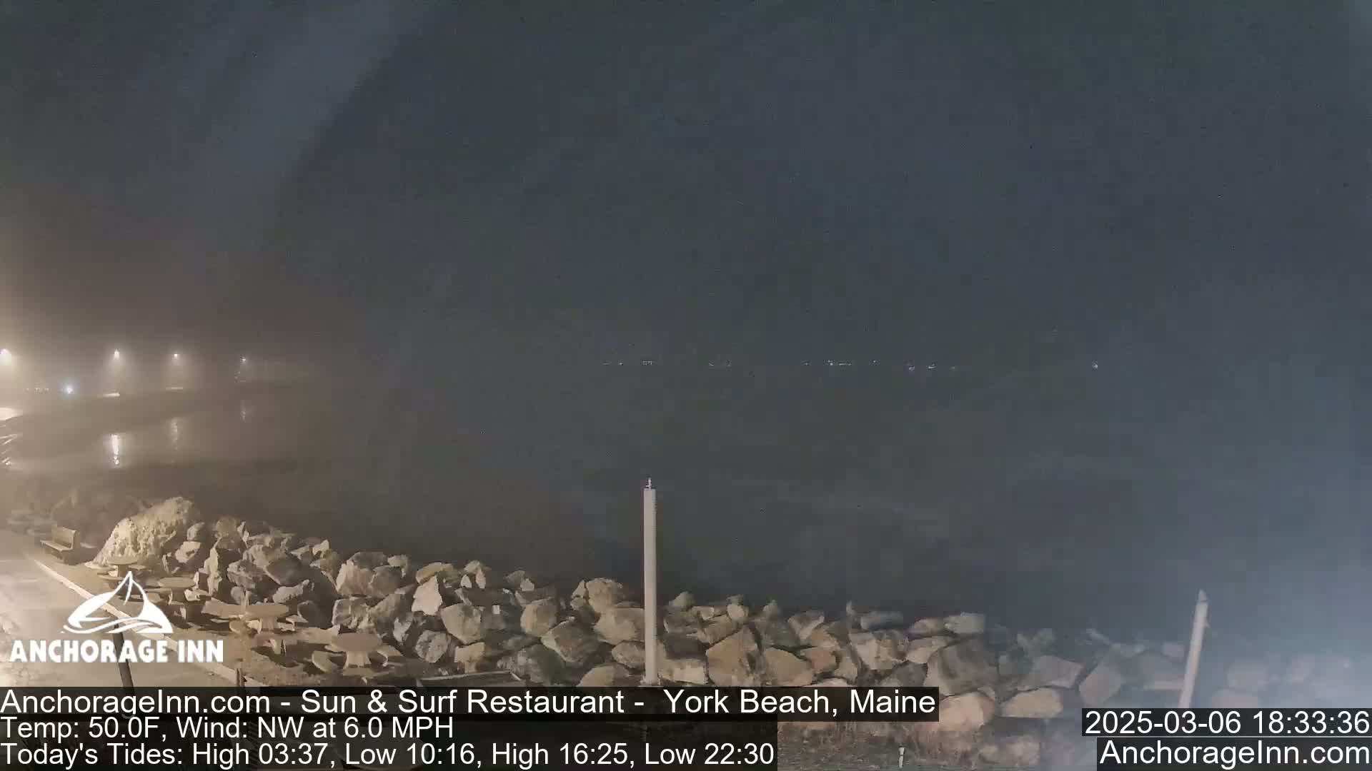 A nighttime, foggy view of a rocky shoreline and calm water.