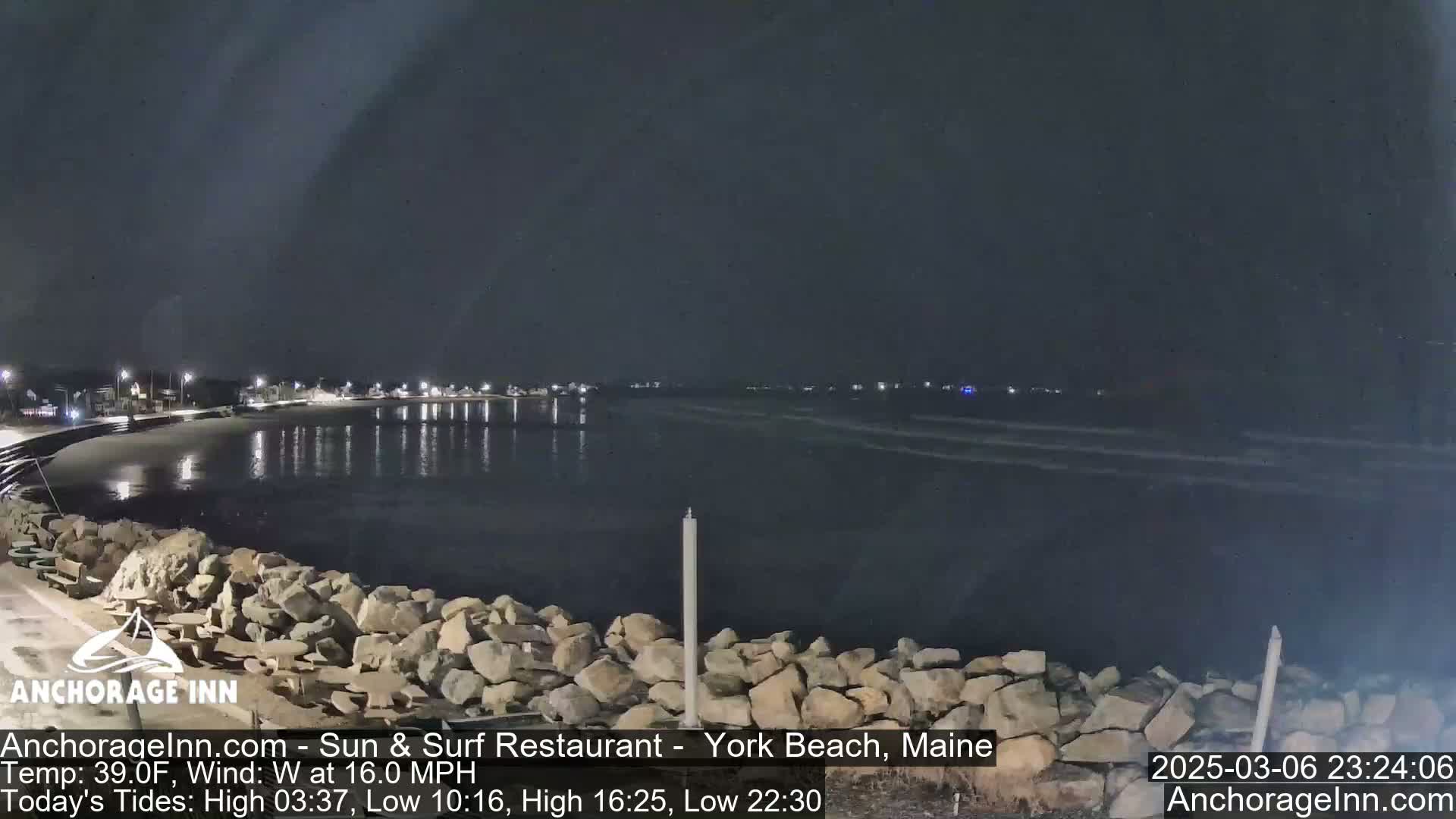 A nighttime view of a rocky shoreline and calm ocean water under a dark sky.