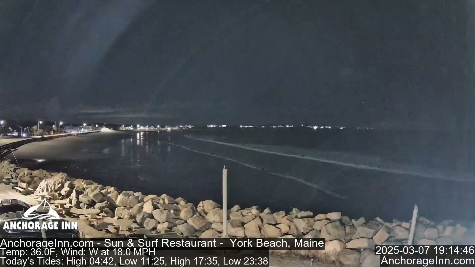 A nighttime view of a rocky shoreline and dark ocean with small waves under a mostly clear sky.