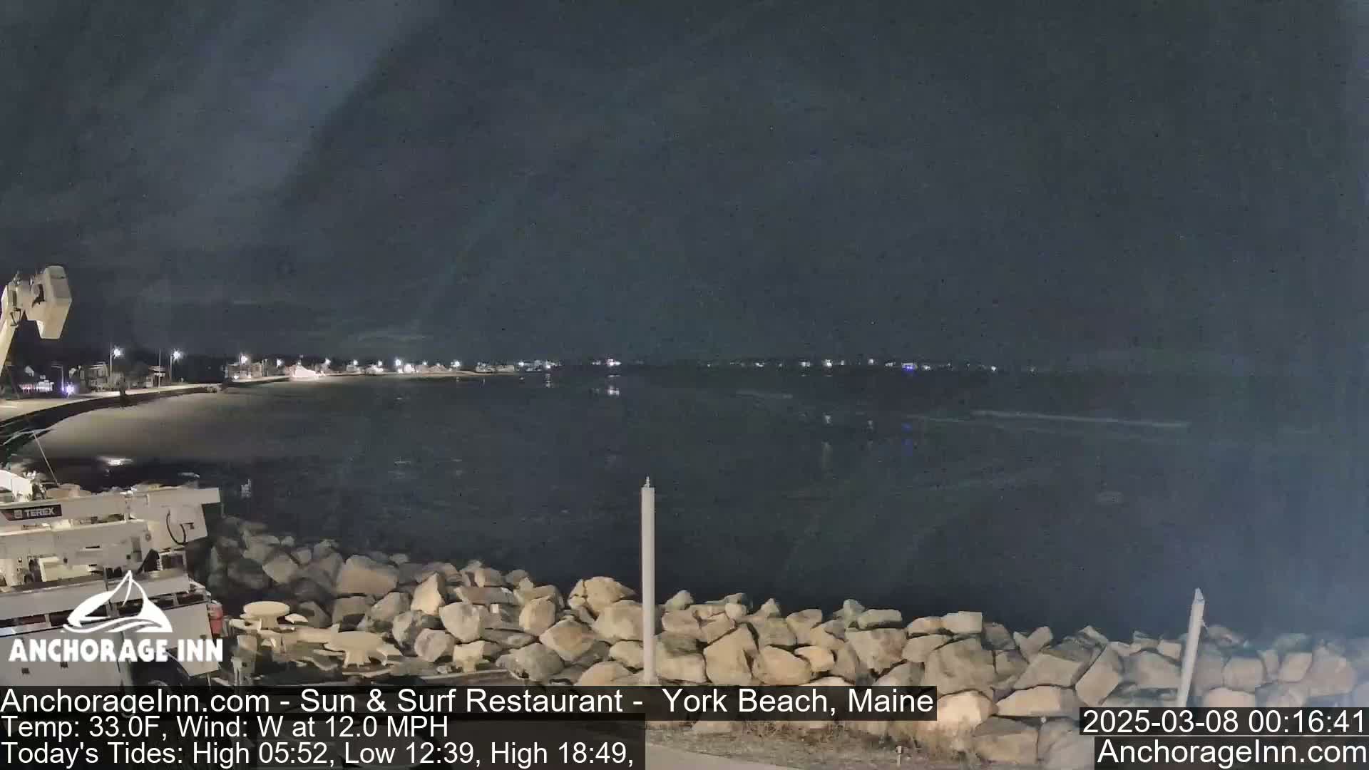 A nighttime view of a calm body of water, a rocky shoreline, and a piece of construction equipment under a dark sky.