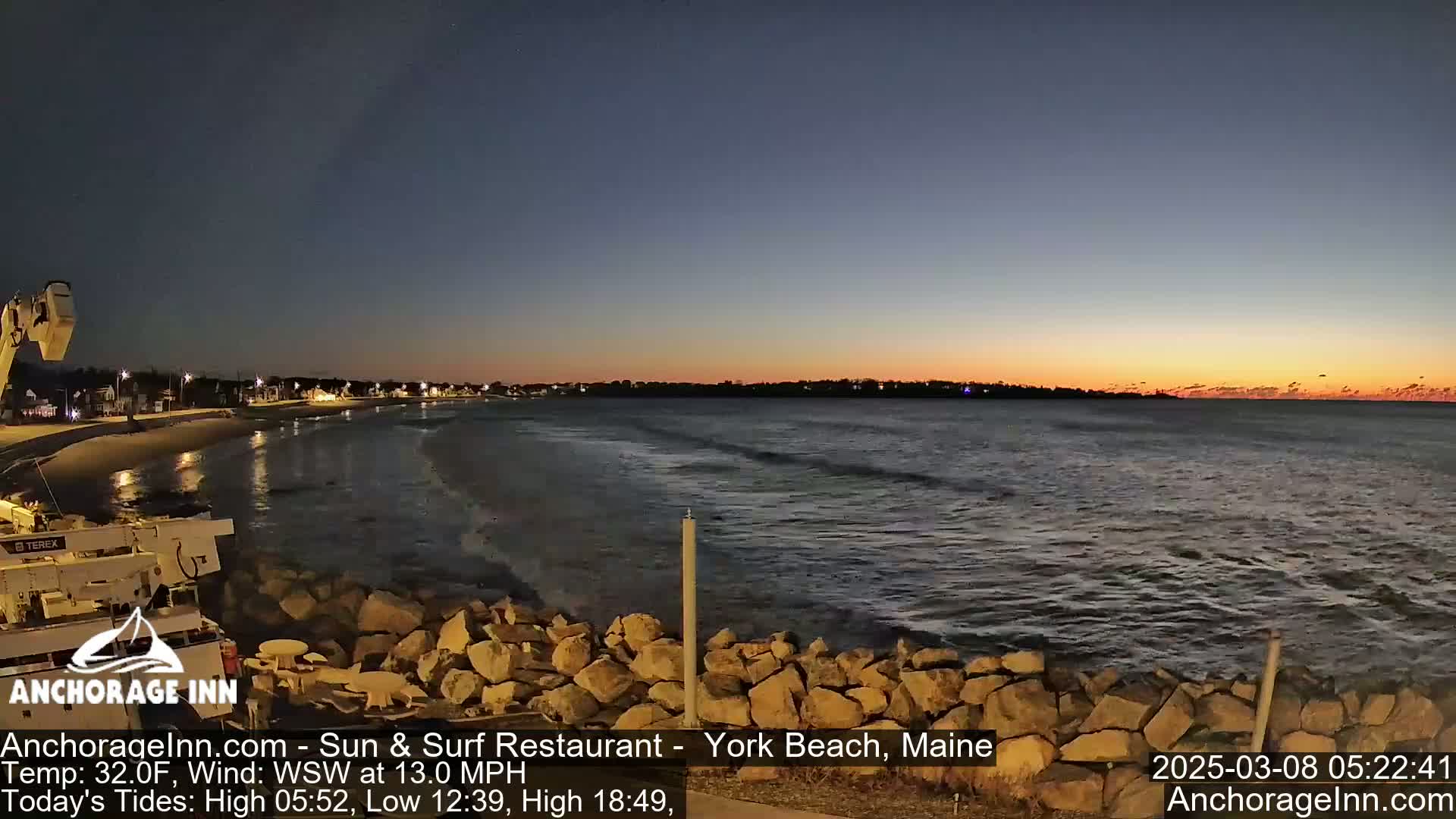 A twilight seaside scene shows a calm ocean with small waves lapping a rocky shore, under a mostly clear sky transitioning from dusk to dawn.