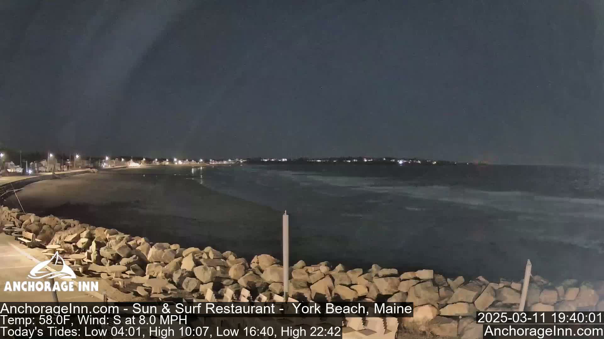 A nighttime view of a rocky shoreline and calm ocean under a dark sky.