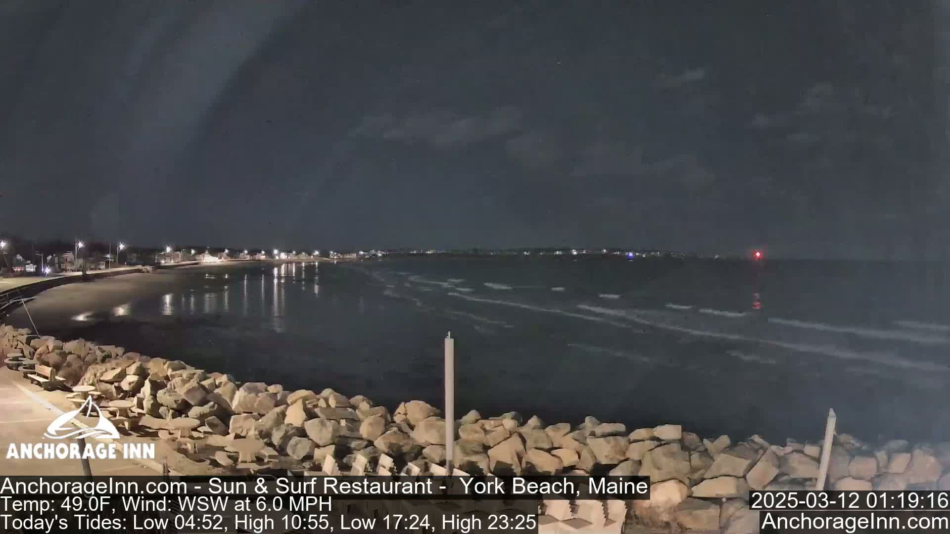 A nighttime view of a rocky shoreline and calm ocean under a dark sky.