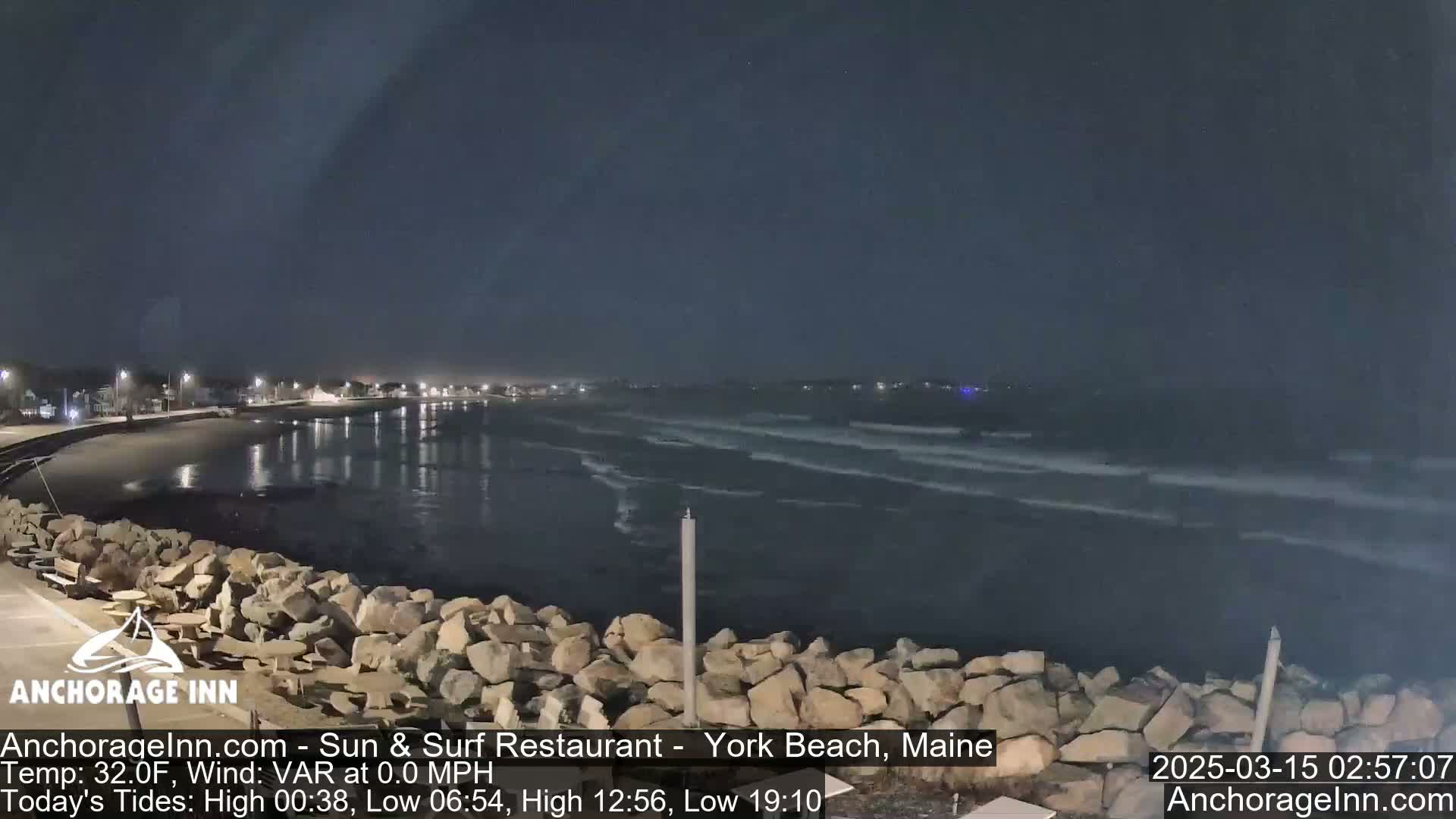 A nighttime view of a rocky shoreline and calm ocean waves under a dark sky.