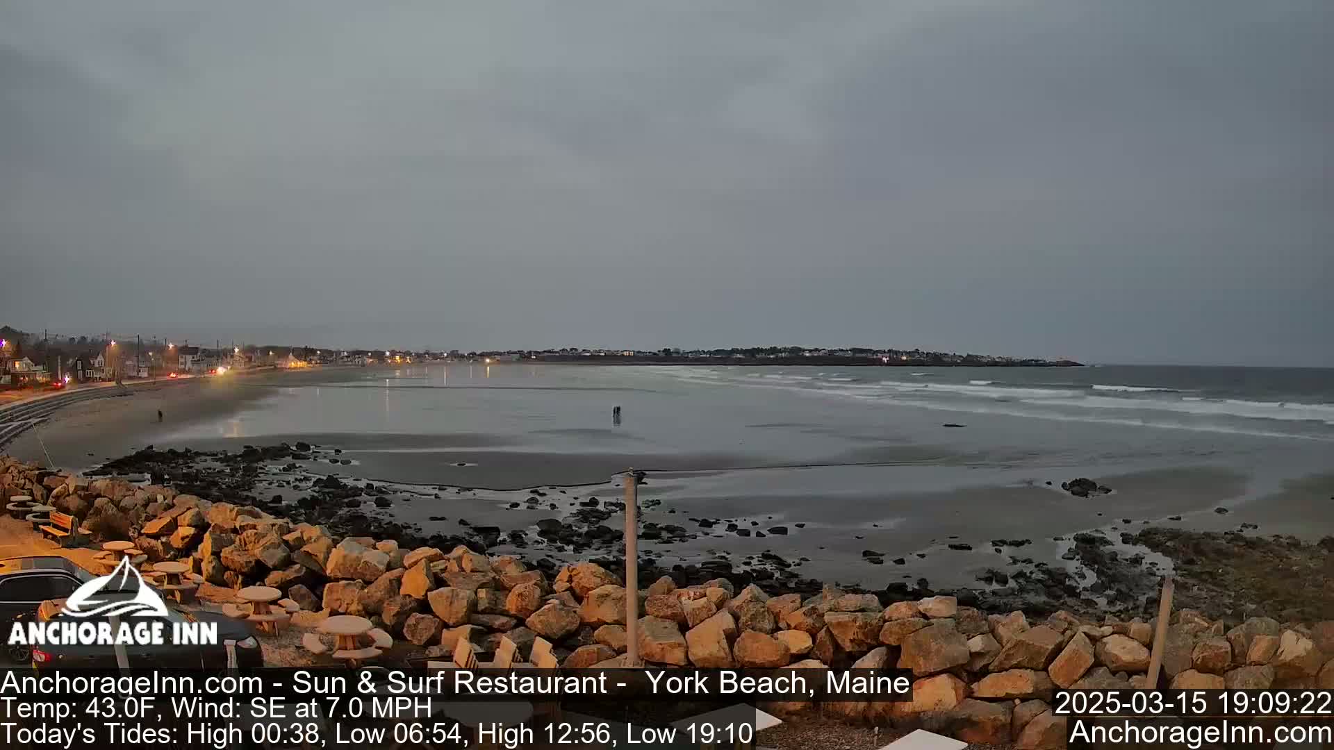 A beach with a rocky shoreline and calm waves under an overcast sky is seen at dusk.