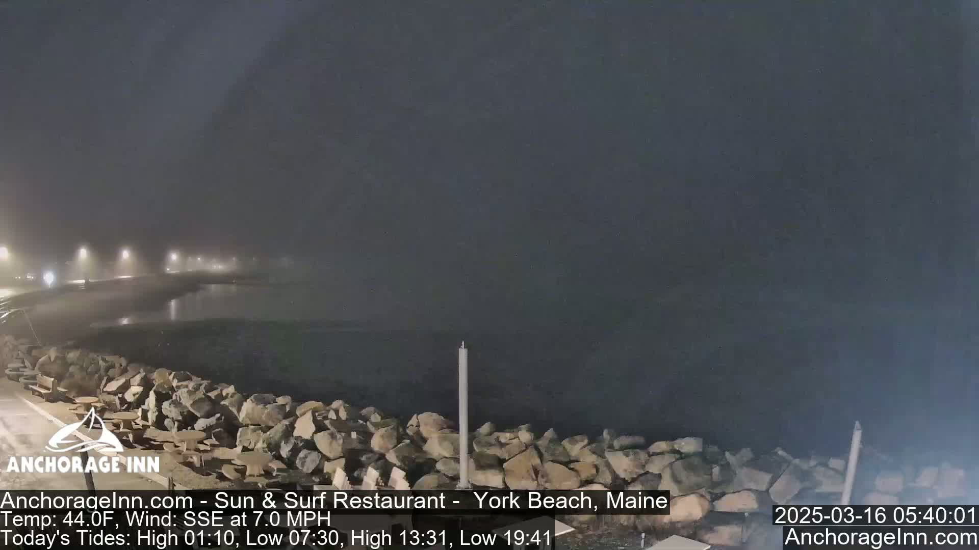 A foggy, nighttime scene shows a rocky shoreline and calm water under dim lighting.