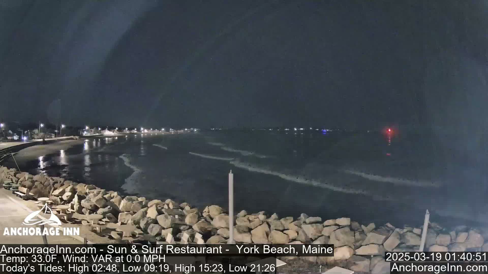 A nighttime view of a rocky shoreline and calm ocean under a dark sky.