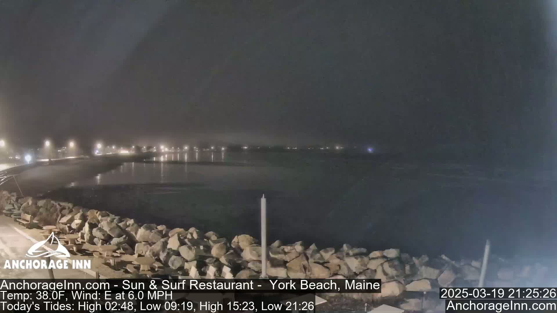 A nighttime view of a calm body of water with a rocky shoreline under hazy conditions.