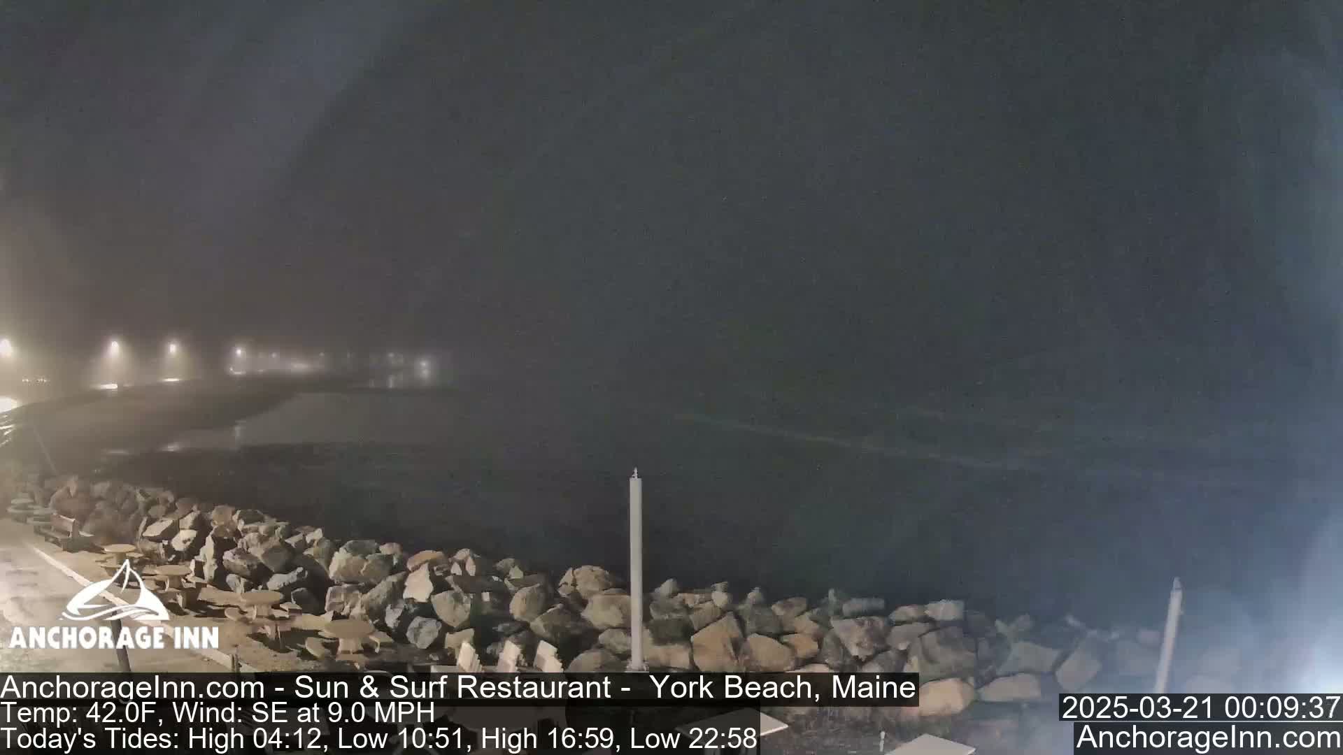 A foggy, nighttime coastal scene shows a rocky shoreline and dark ocean water under dim lighting.