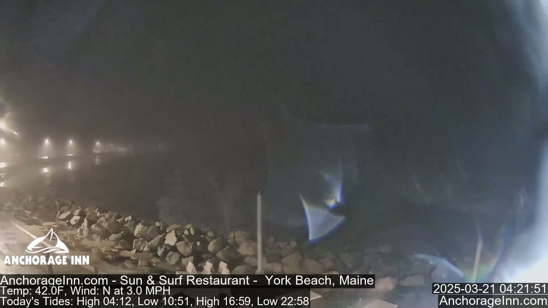 A foggy nighttime scene shows a rocky shoreline and dimly lit area beyond.