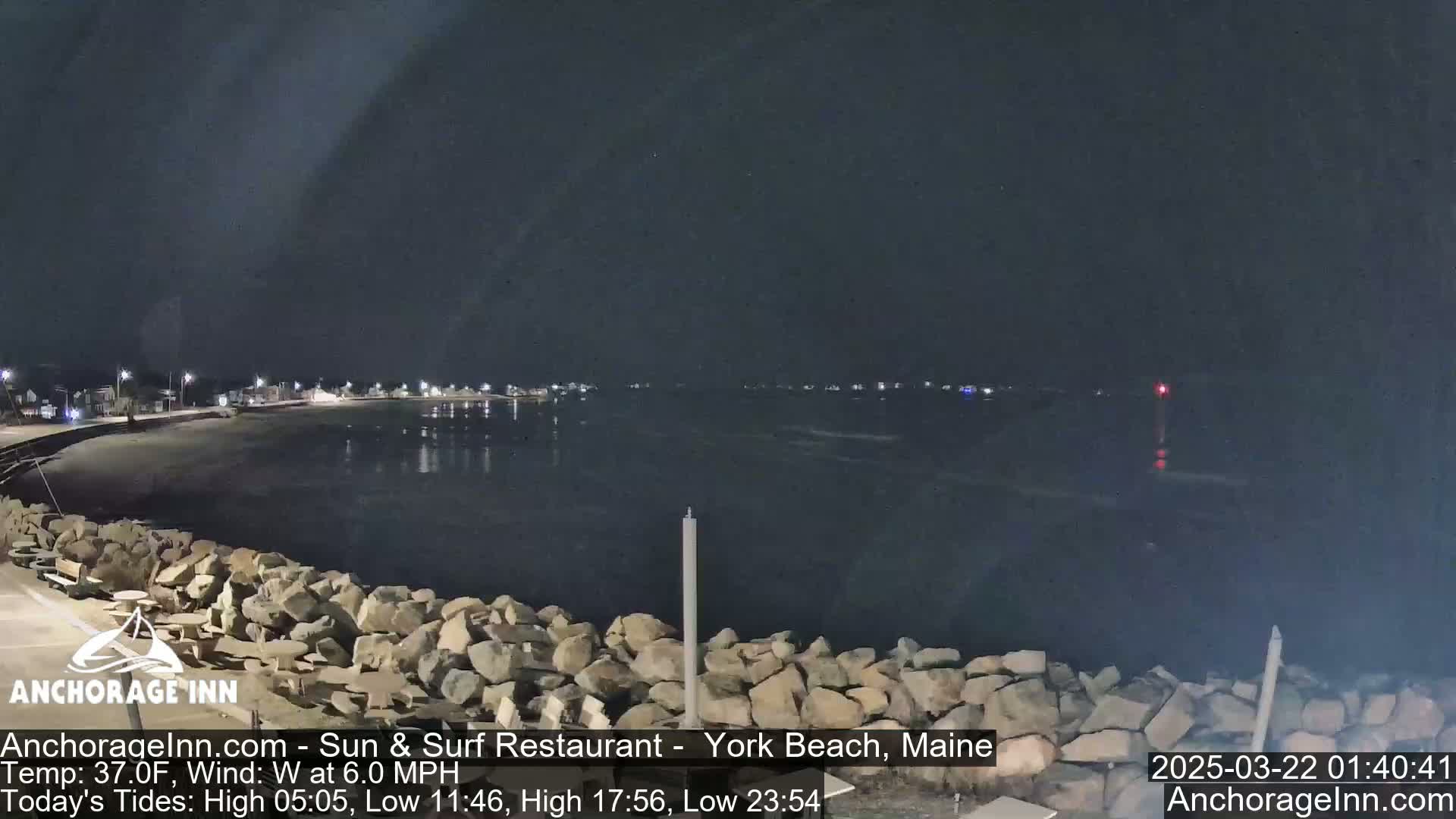 A nighttime view of a calm body of water, partially enclosed by a rocky shoreline, under a dark sky.
