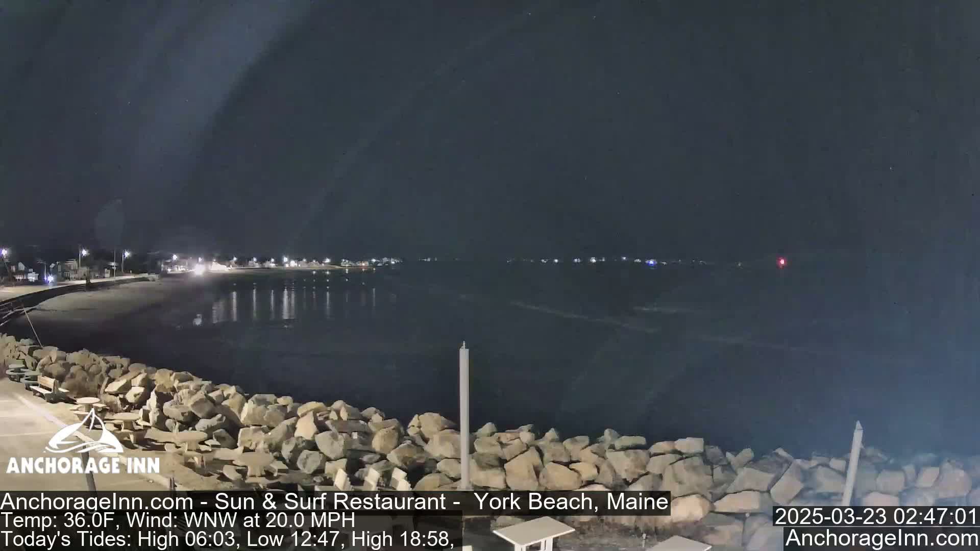A nighttime view of a rocky shoreline and calm ocean under a dark sky.