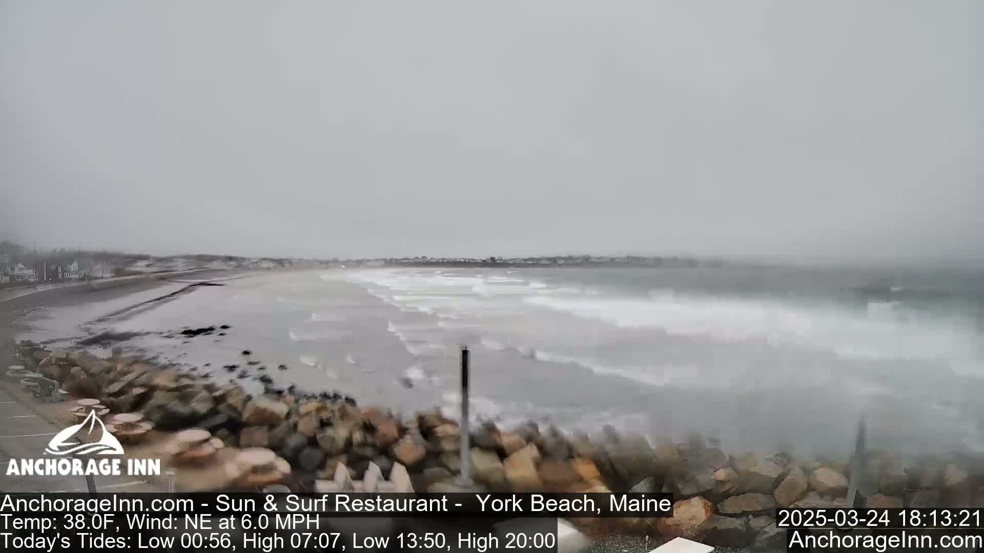 A rocky shoreline with choppy waves crashing against it during an overcast day.