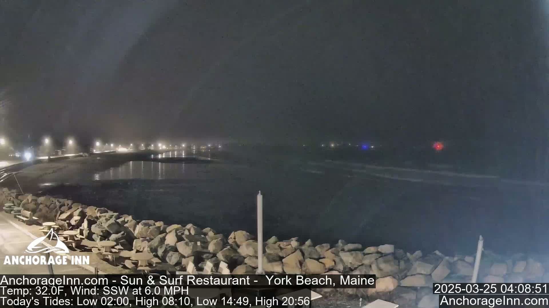 A nighttime view of a rocky shoreline and calm ocean under a hazy sky.