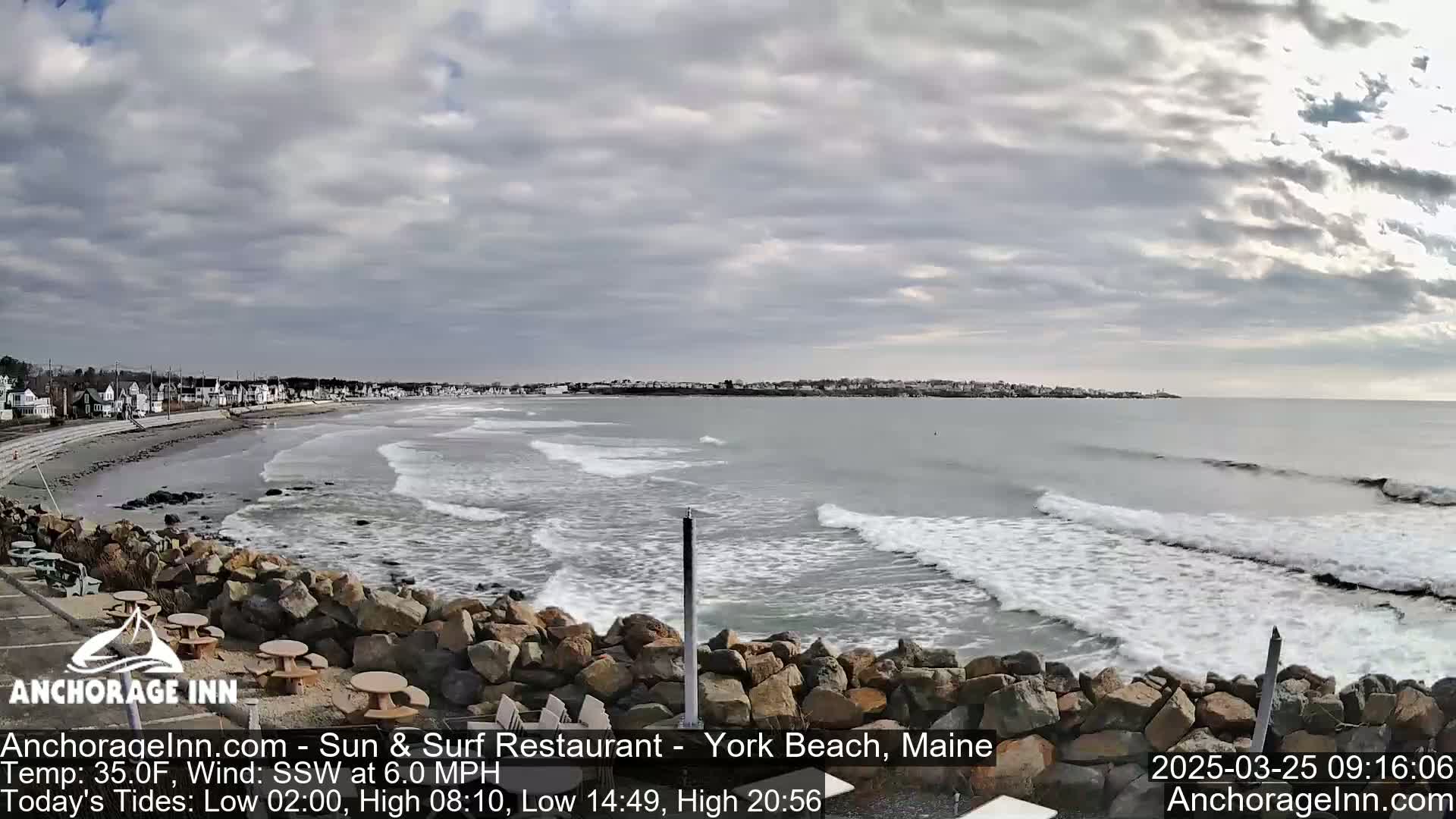 A rocky shoreline overlooks a beach with gentle waves under a mostly cloudy sky.
