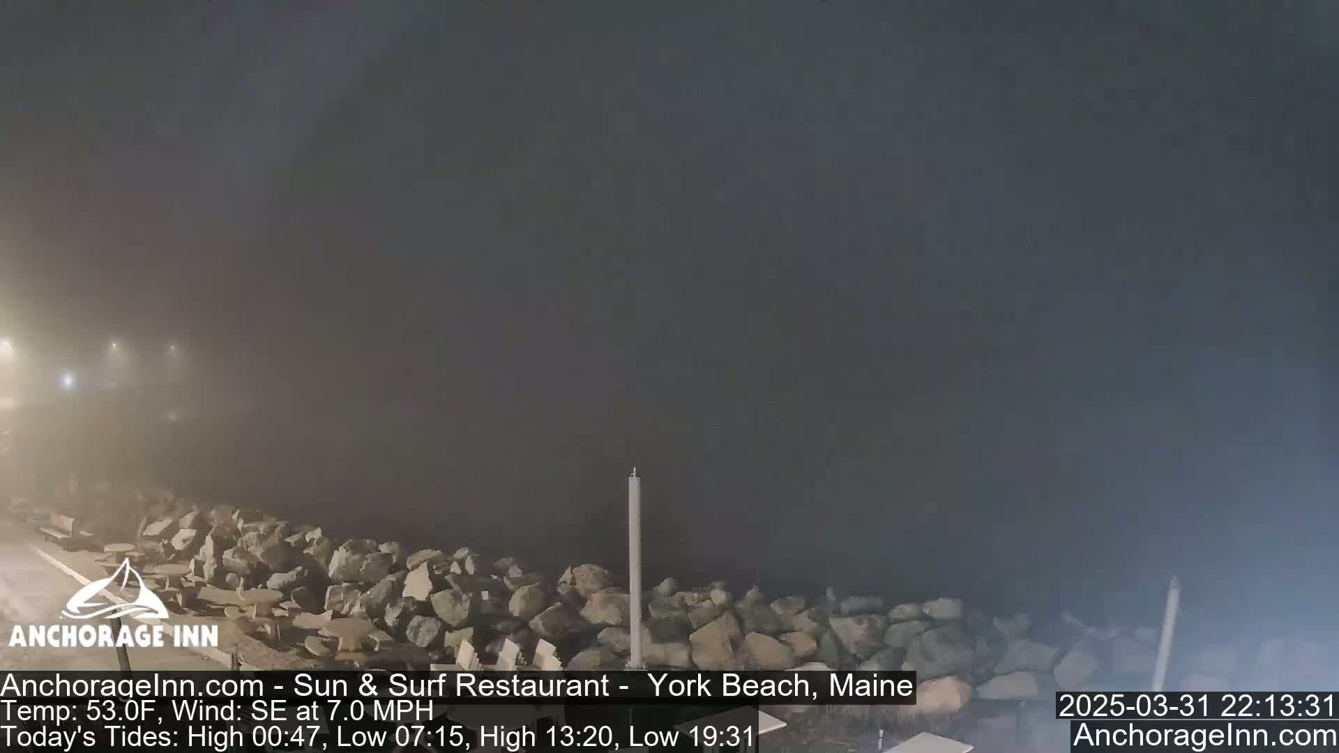 A foggy nighttime scene shows a rocky shoreline with a single tall pole standing near the water's edge.