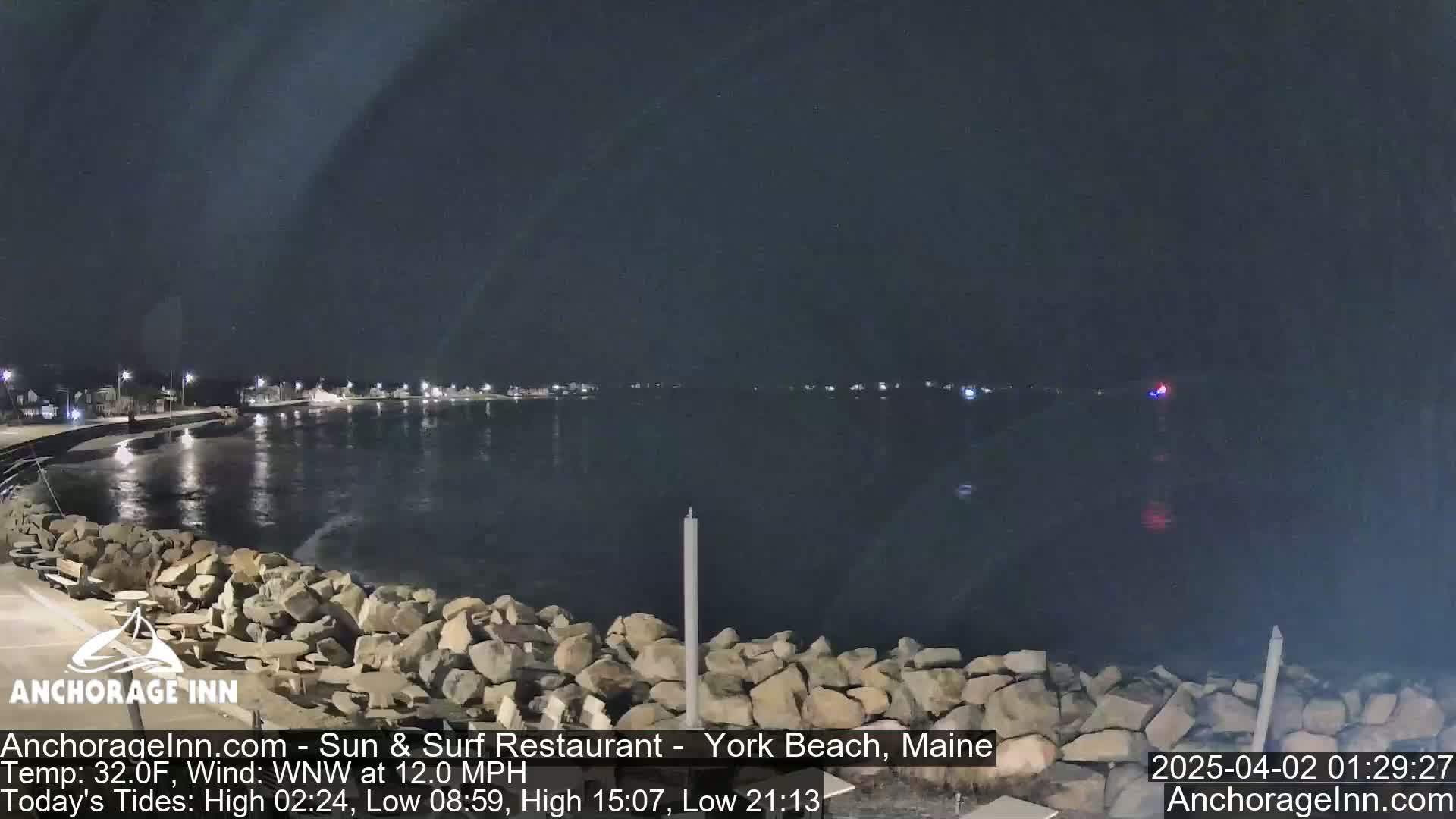 A nighttime view of a rocky shoreline and calm body of water, under a dark sky.