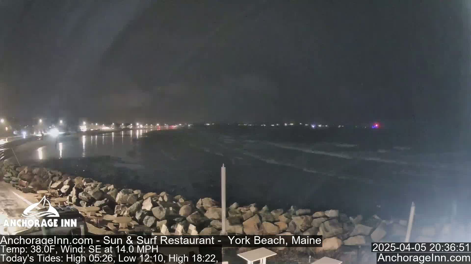 A nighttime view of a rocky shoreline with a dark, choppy ocean under a cloudy sky.