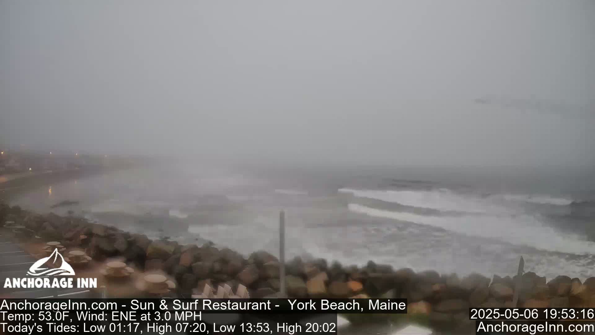 A foggy, overcast day shows a rocky shoreline with choppy waves crashing against it.