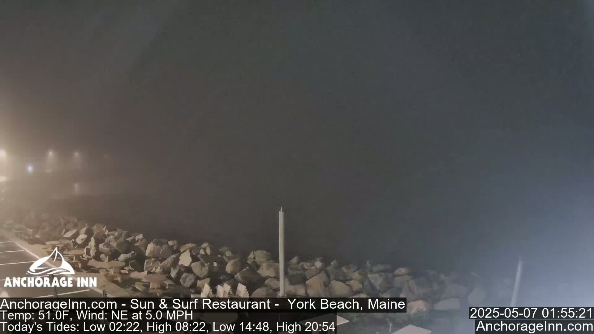 A foggy nighttime scene shows a rocky shoreline with a tall pole near the center.