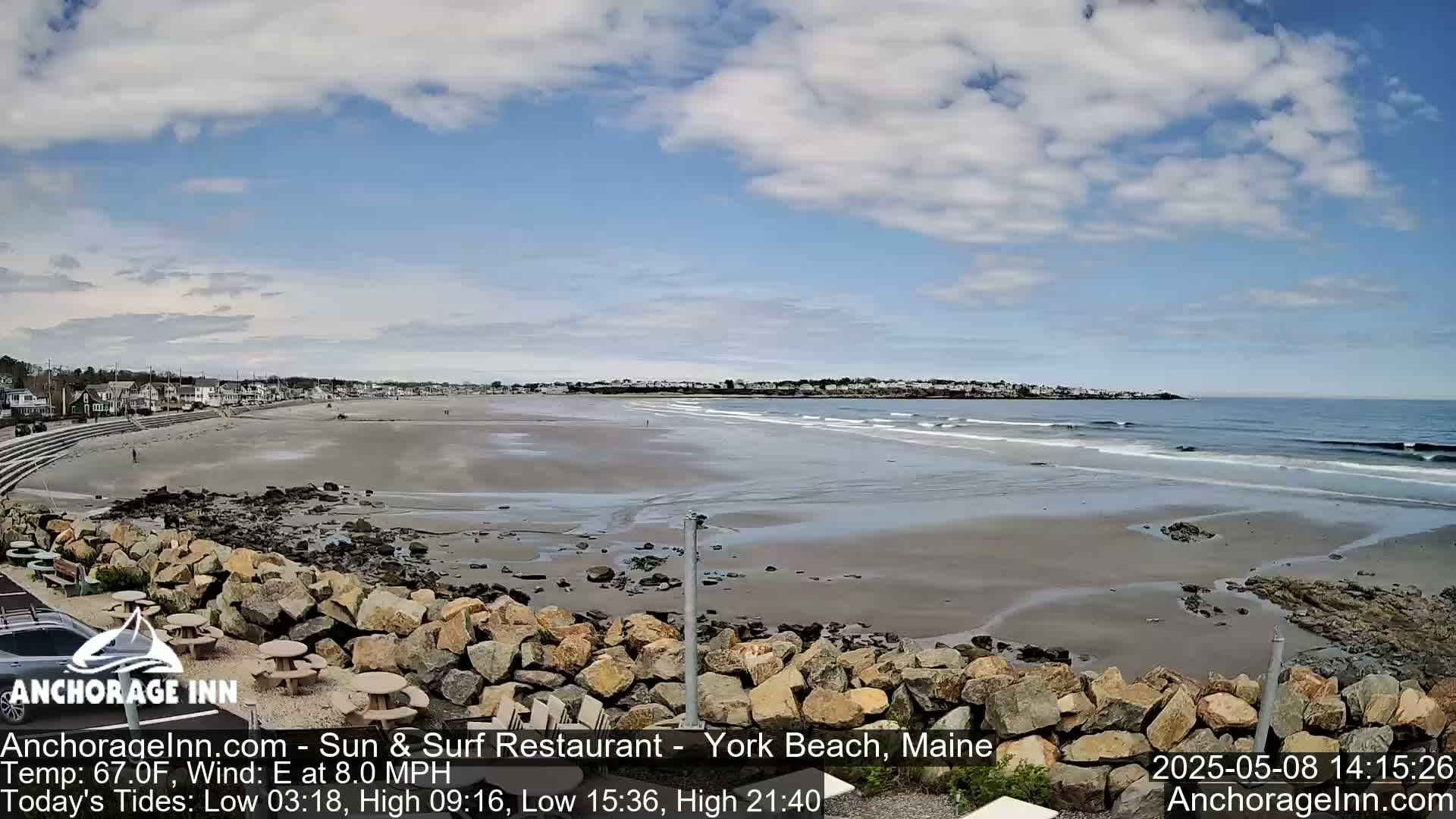 A sandy beach with small waves stretches out to the ocean under a partly cloudy blue sky.