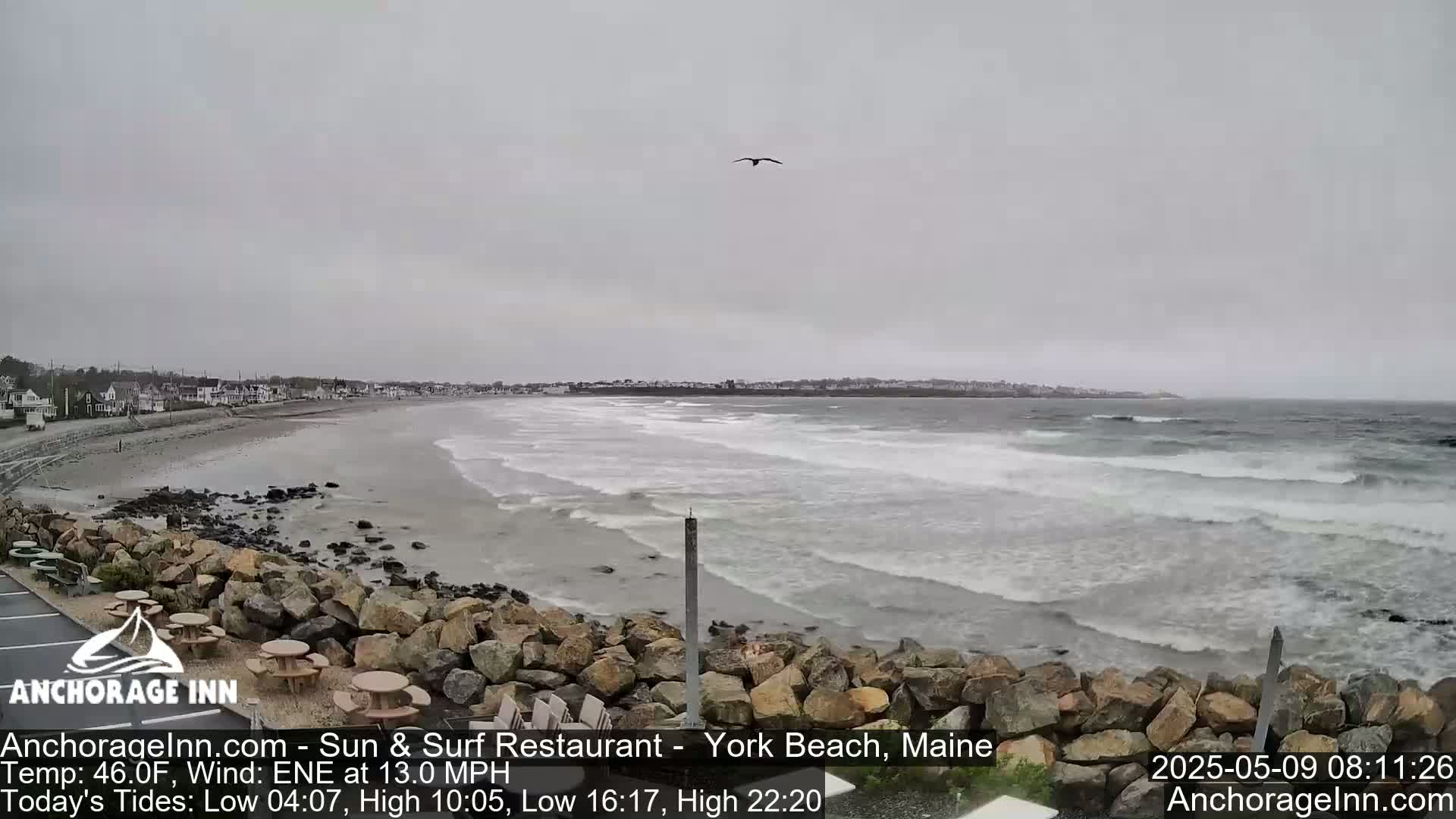 A rocky shoreline overlooks a beach with moderate waves under an overcast sky.